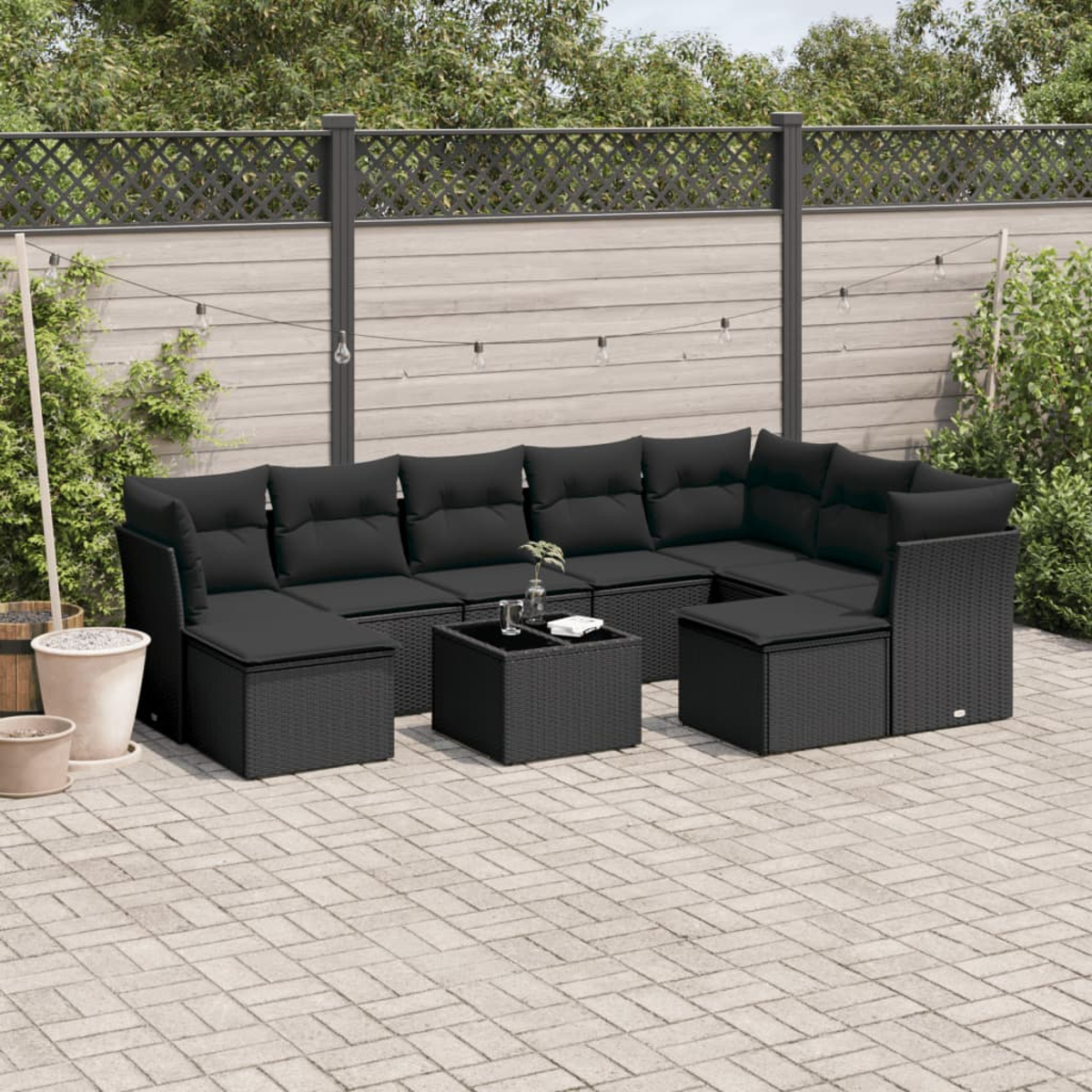 Outdoor-Sofa-Set aus schwarzem Rattan mit schwarzen Kissen, Tisch, auf einer Terrasse. Zaun im Hintergrund.