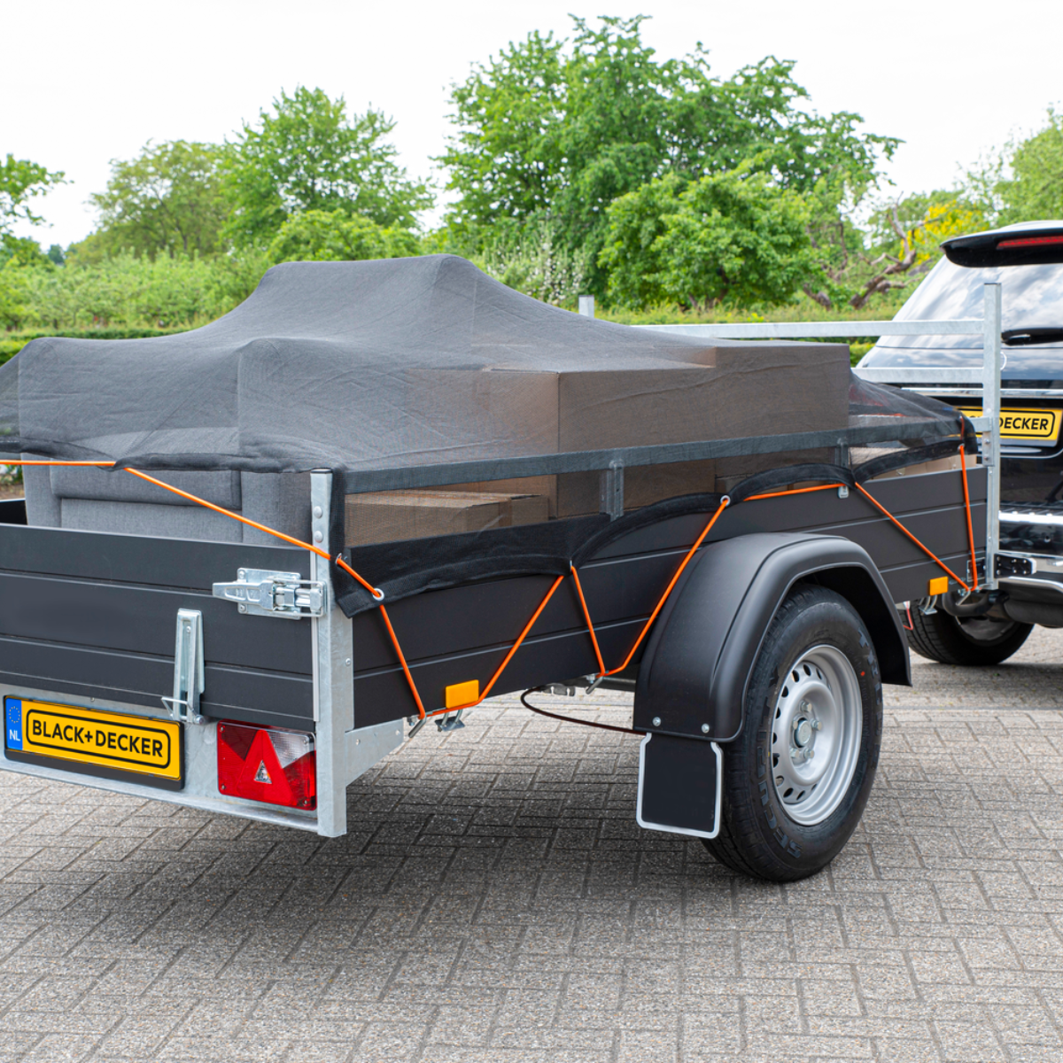 Zwarte aanhanger met een grijs gaasnet, aangekoppeld aan een zwarte auto.
