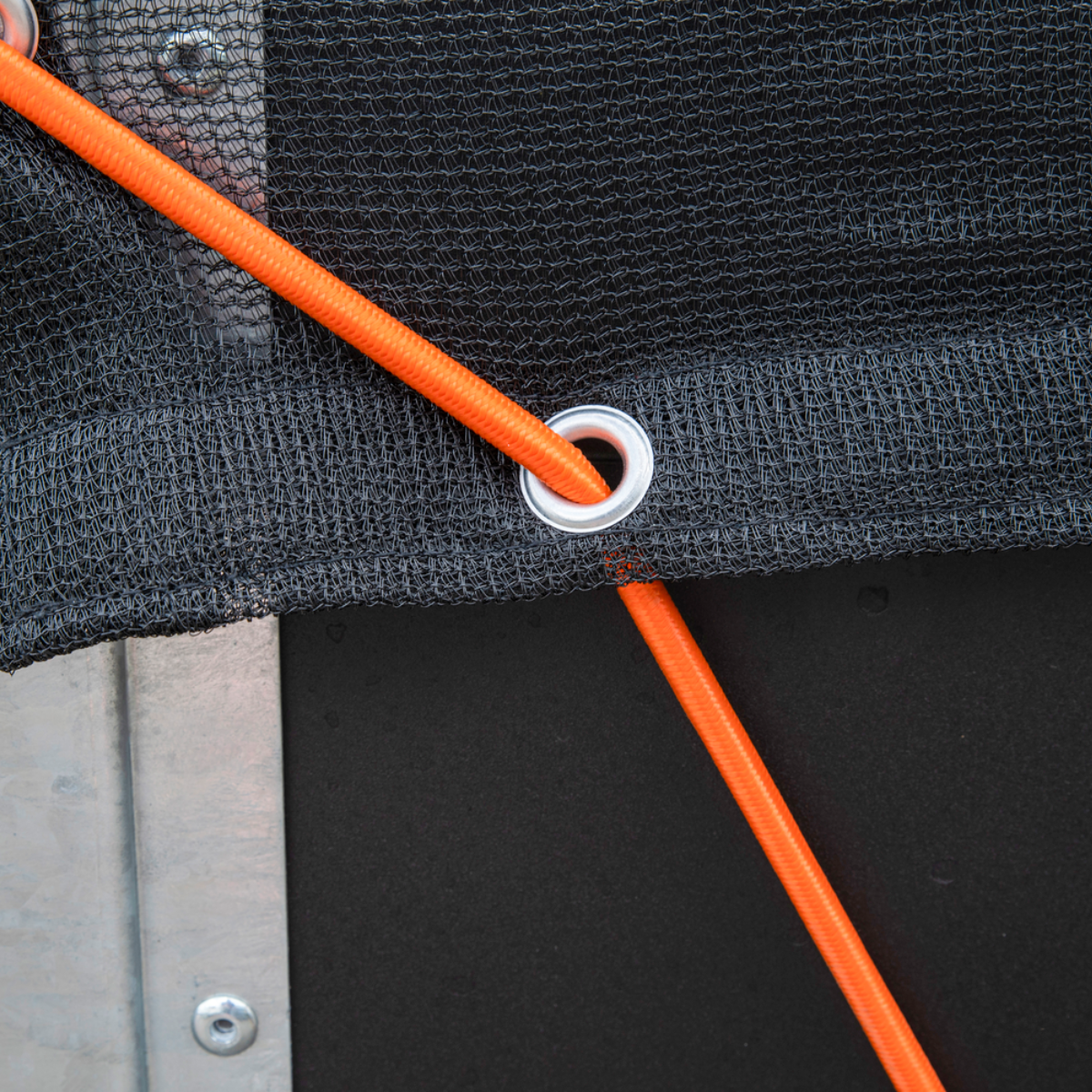 Close-up van een oranje touw dat door een metalen oog in zwart net is geregen. Het net is tegen een donkere achtergrond.