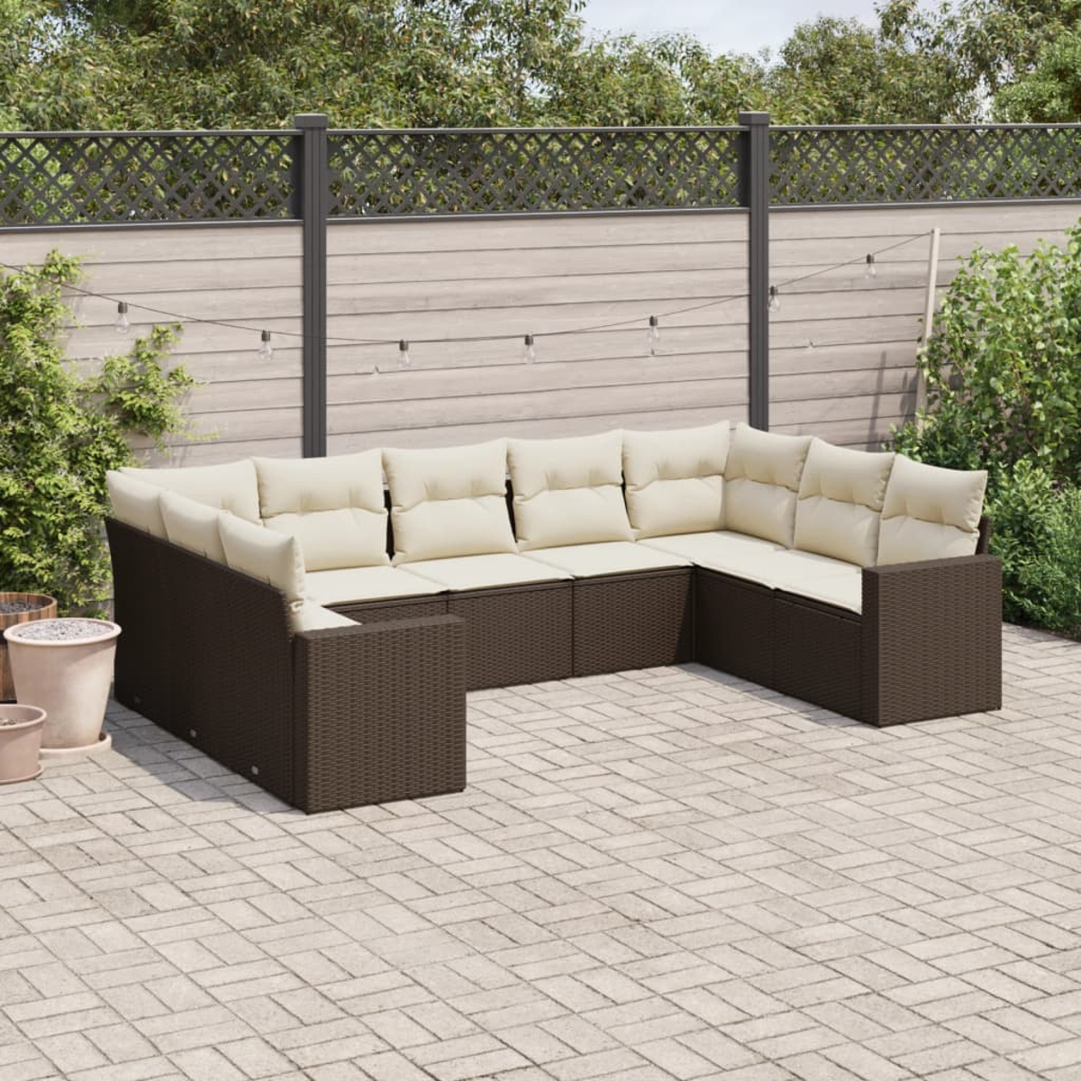 Braunes Ecksofa aus Korbgeflecht mit cremefarbenen Kissen, auf einer gepflasterten Terrasse mit Grün umgeben.