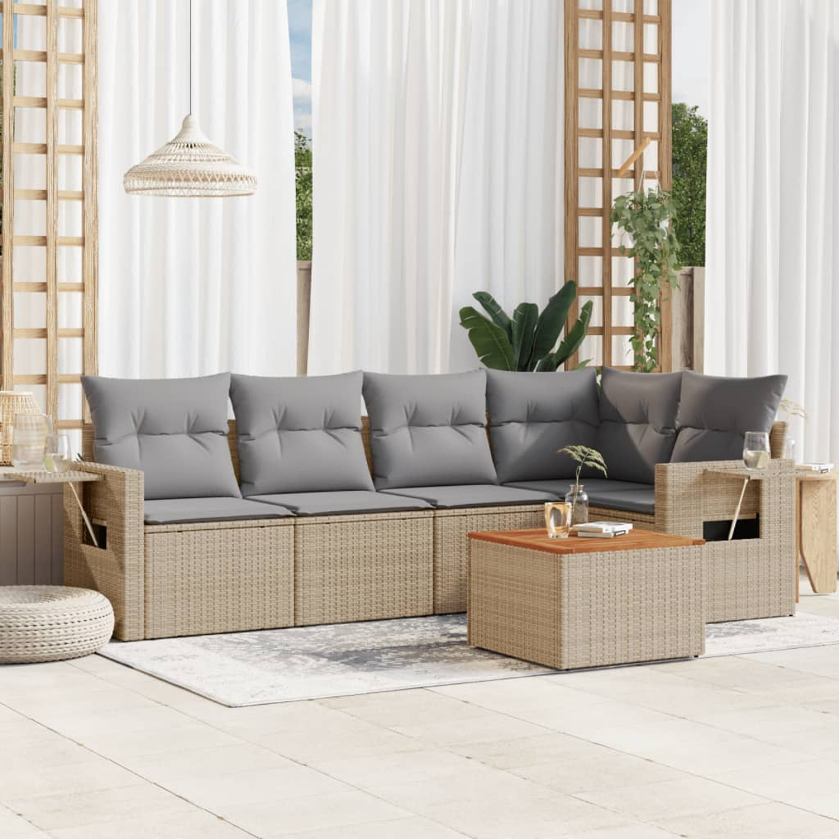 Rattan-Sofagarnitur für den Außenbereich mit Holztisch. Auf einer weißen Terrasse mit Teppich und cremefarbenen Kissen.