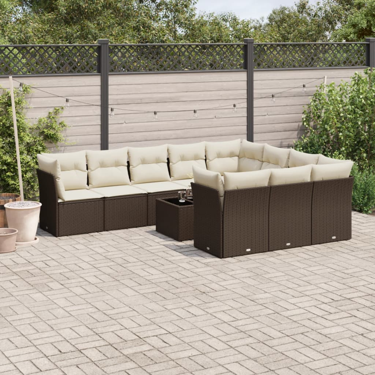 Divano componibile da esterno con cuscini color crema. Patio pavimentato. Recinzione in legno e piante sullo sfondo.