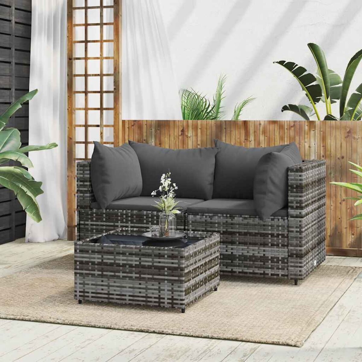 Rattan-Garnitur mit grauen Kissen und Glastisch auf beigem Teppich.