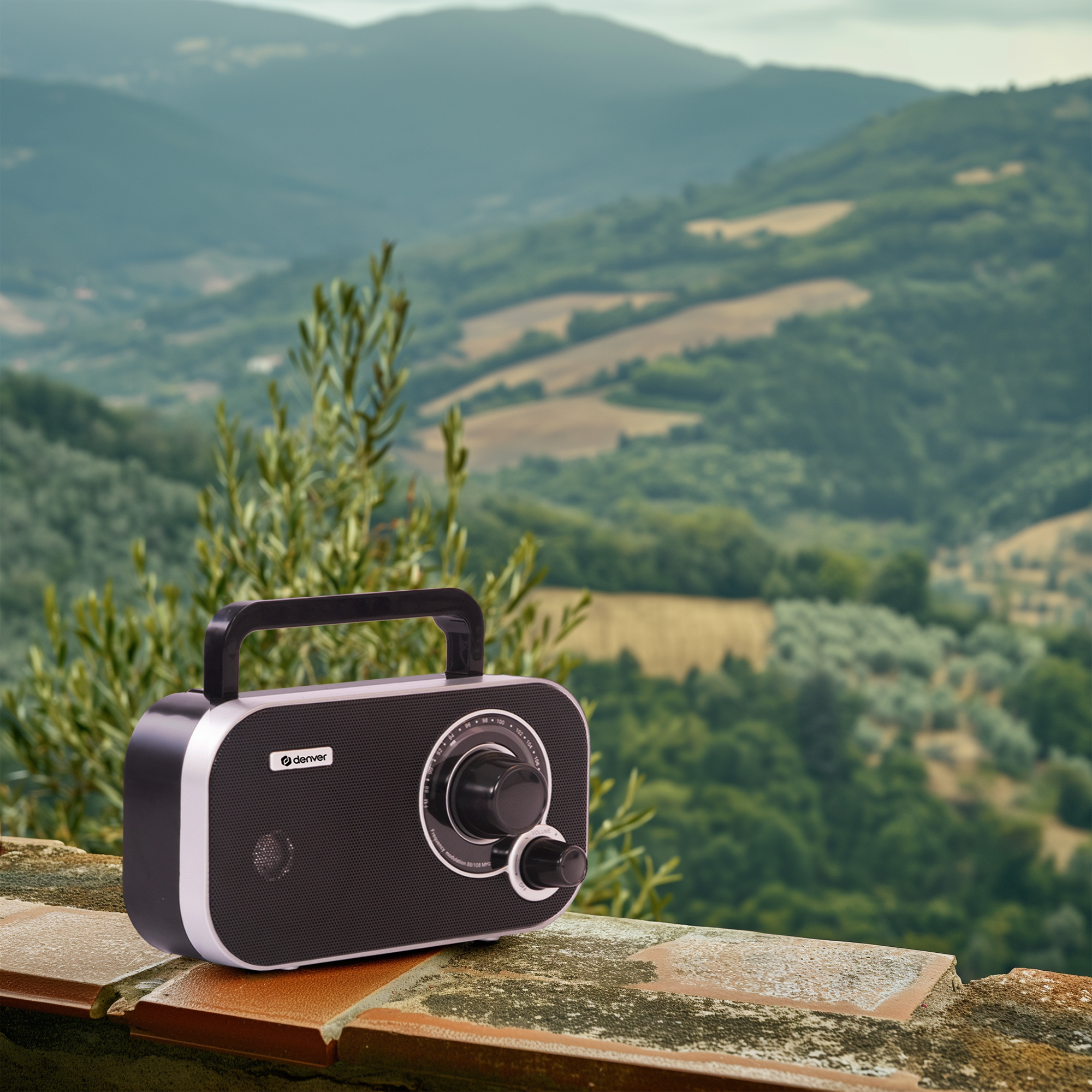Przenośne radio na murze, z zielonym, pagórkowatym krajobrazem w tle.