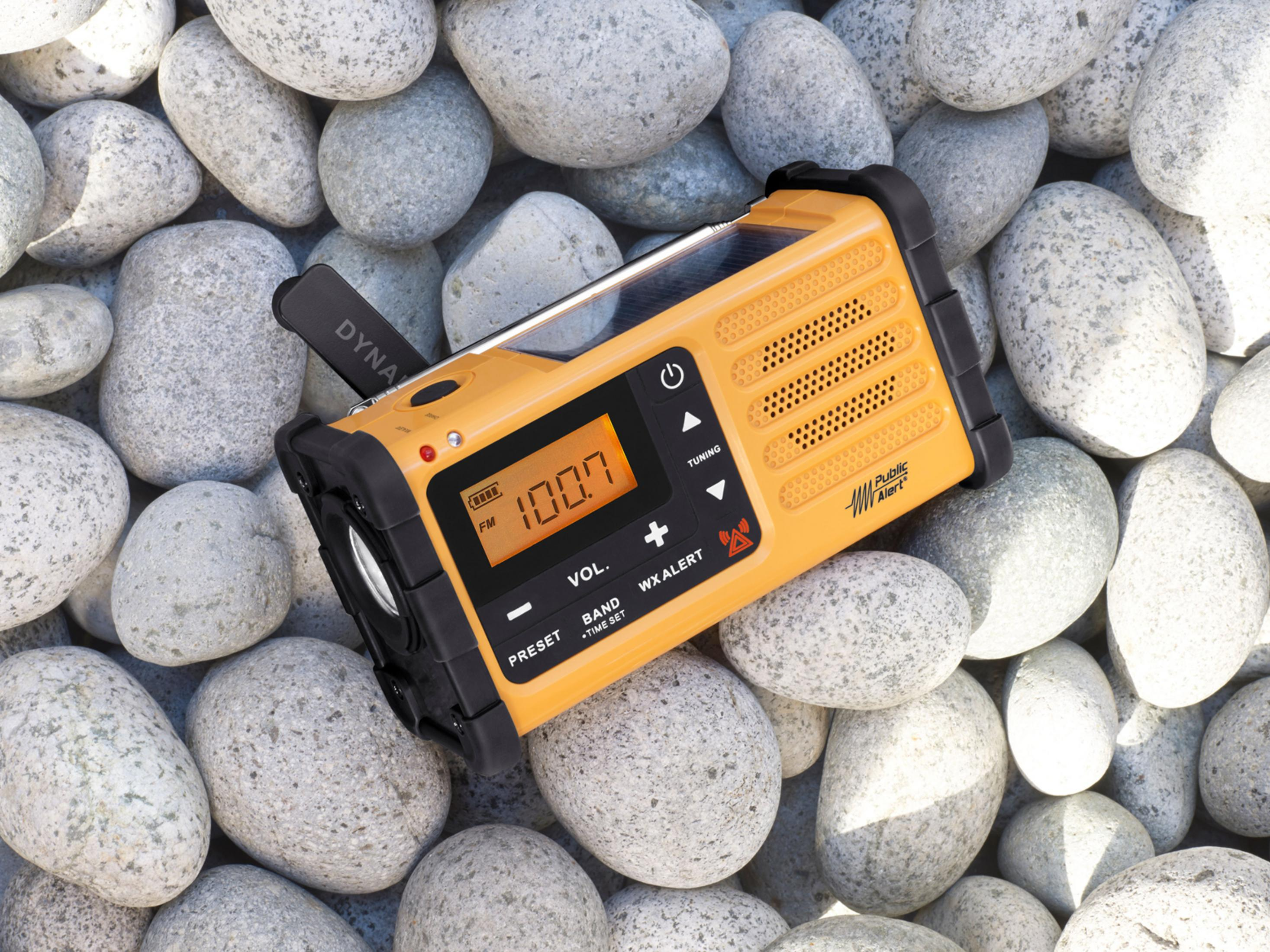 Una radio di emergenza gialla e nera su un letto di pietre grigie, con display digitale.
