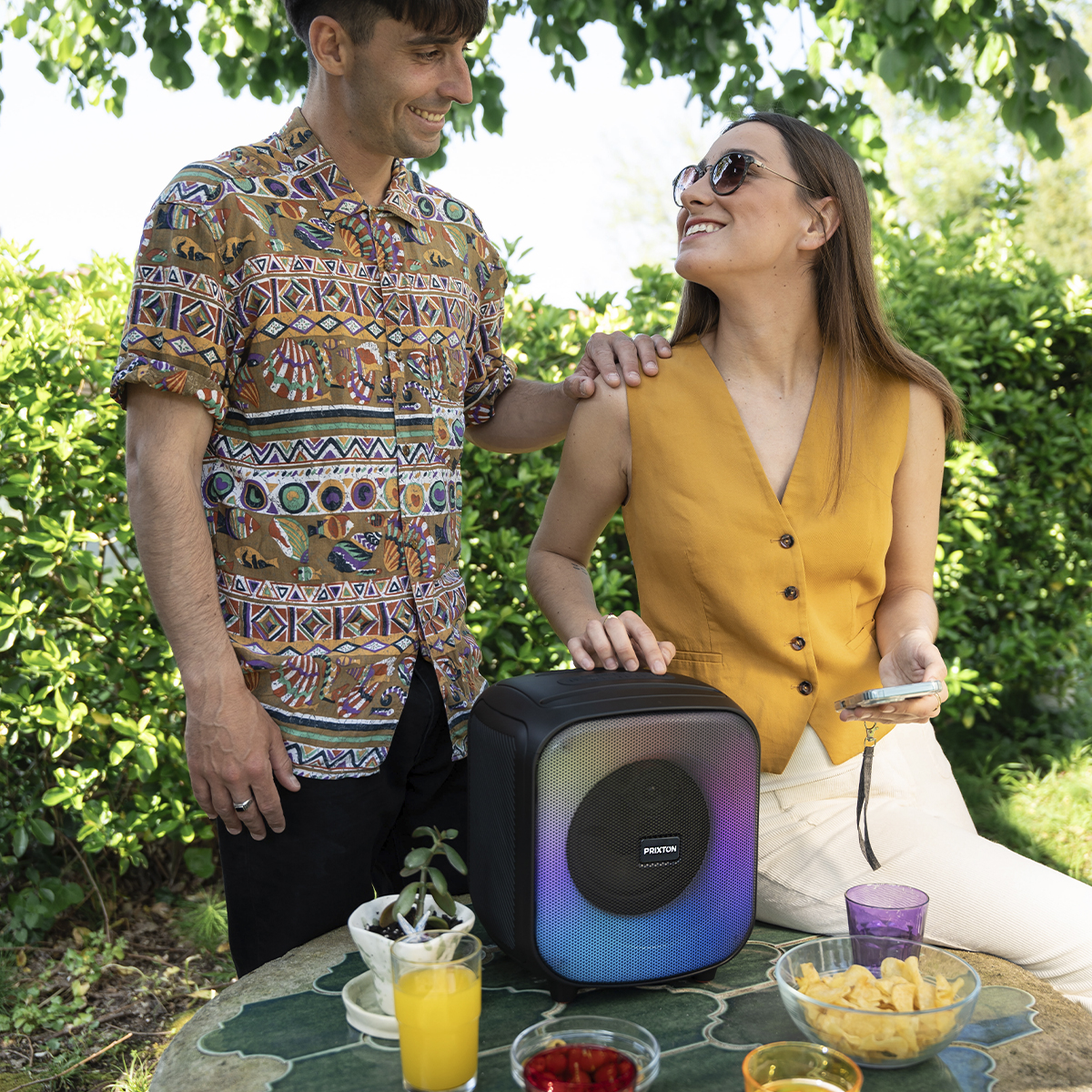 Para słuchająca muzyki. Mężczyzna w koszuli w nadruki i kobieta w żółtej kamizelce, z głośnikiem.