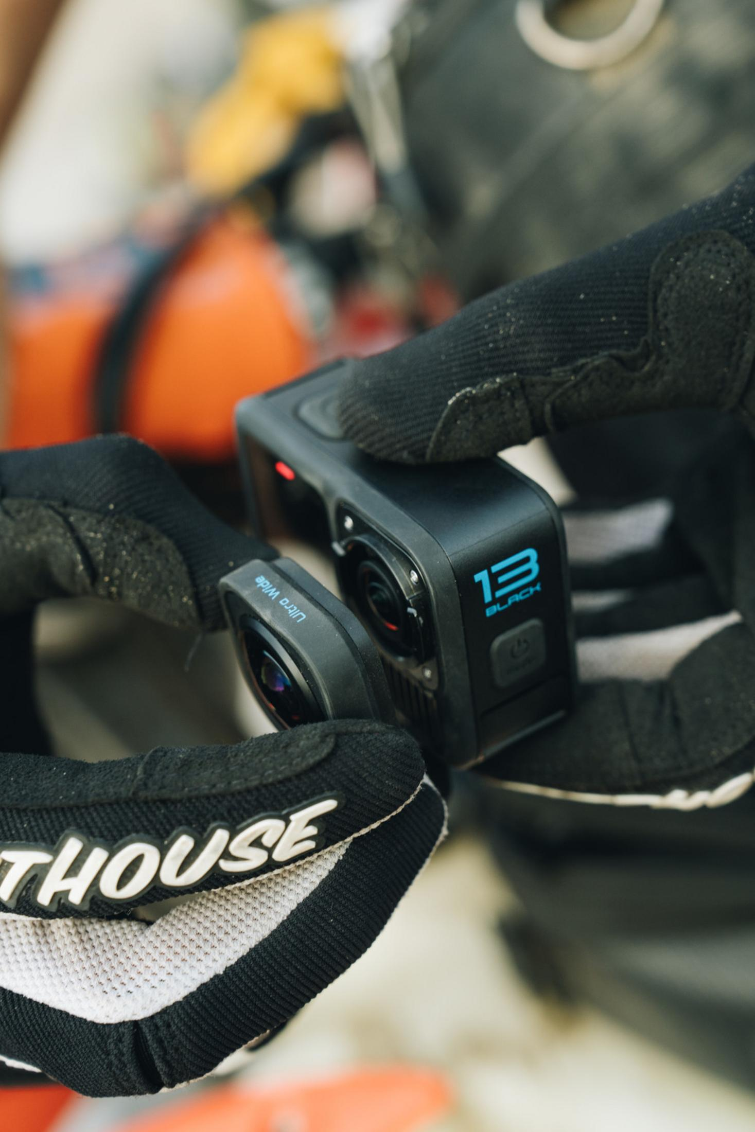 Ręce trzymają czarną kamerę sportową i nakładkę na obiektyw ultraszerokokątny. Noszone są rękawice.