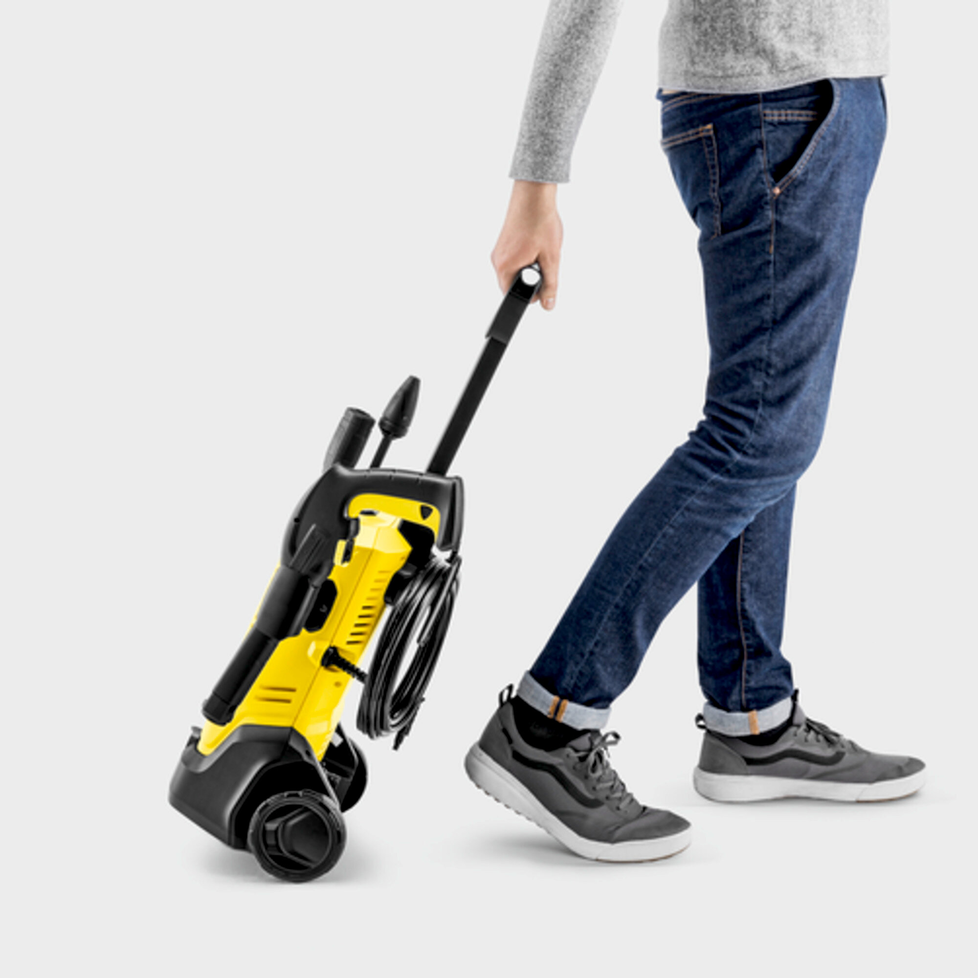 Person carrying a yellow and black pressure washer on wheels. They are wearing jeans and sneakers.
