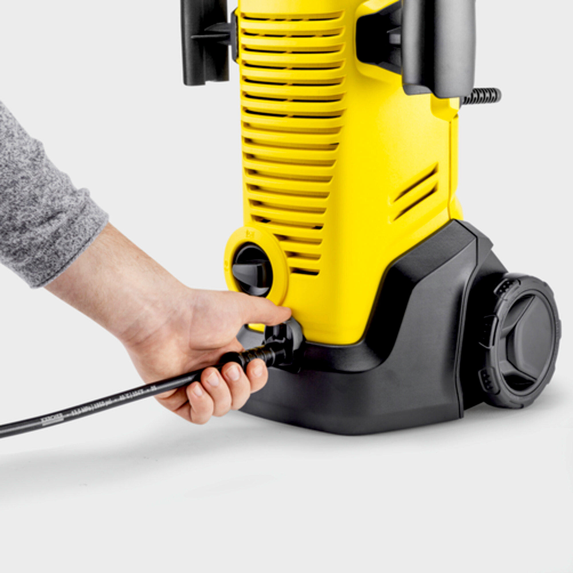 A person's hand connecting a black hose to a yellow pressure washer.