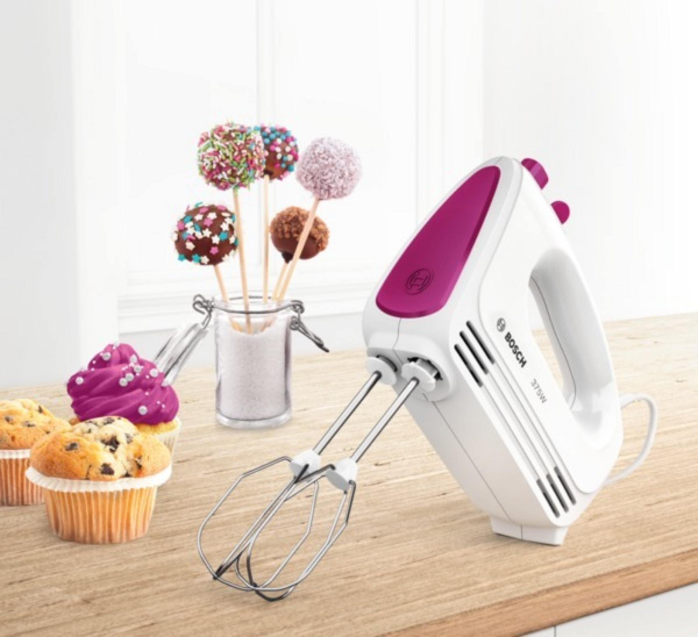 Handrührgerät mit Cupcakes und Cake Pops auf Holzoberfläche.