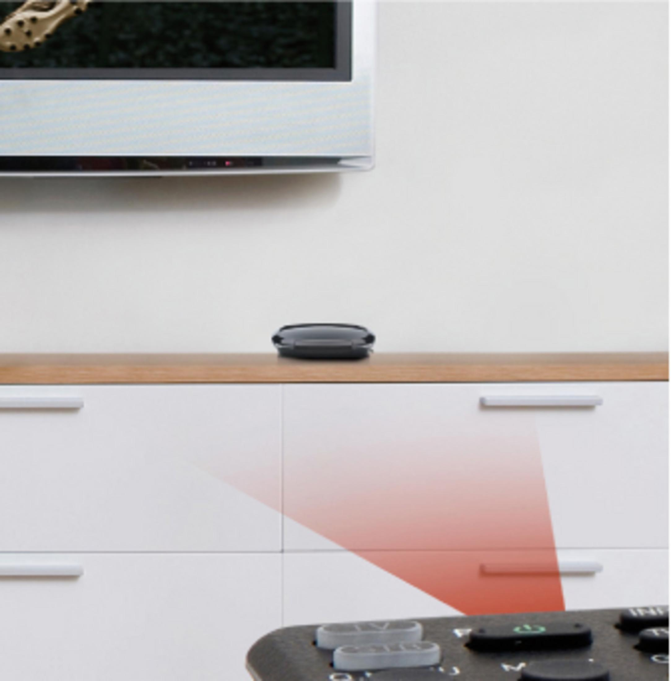 Dispositivo nero su una superficie in legno, sopra un televisore. Una luce rossa indica un segnale.