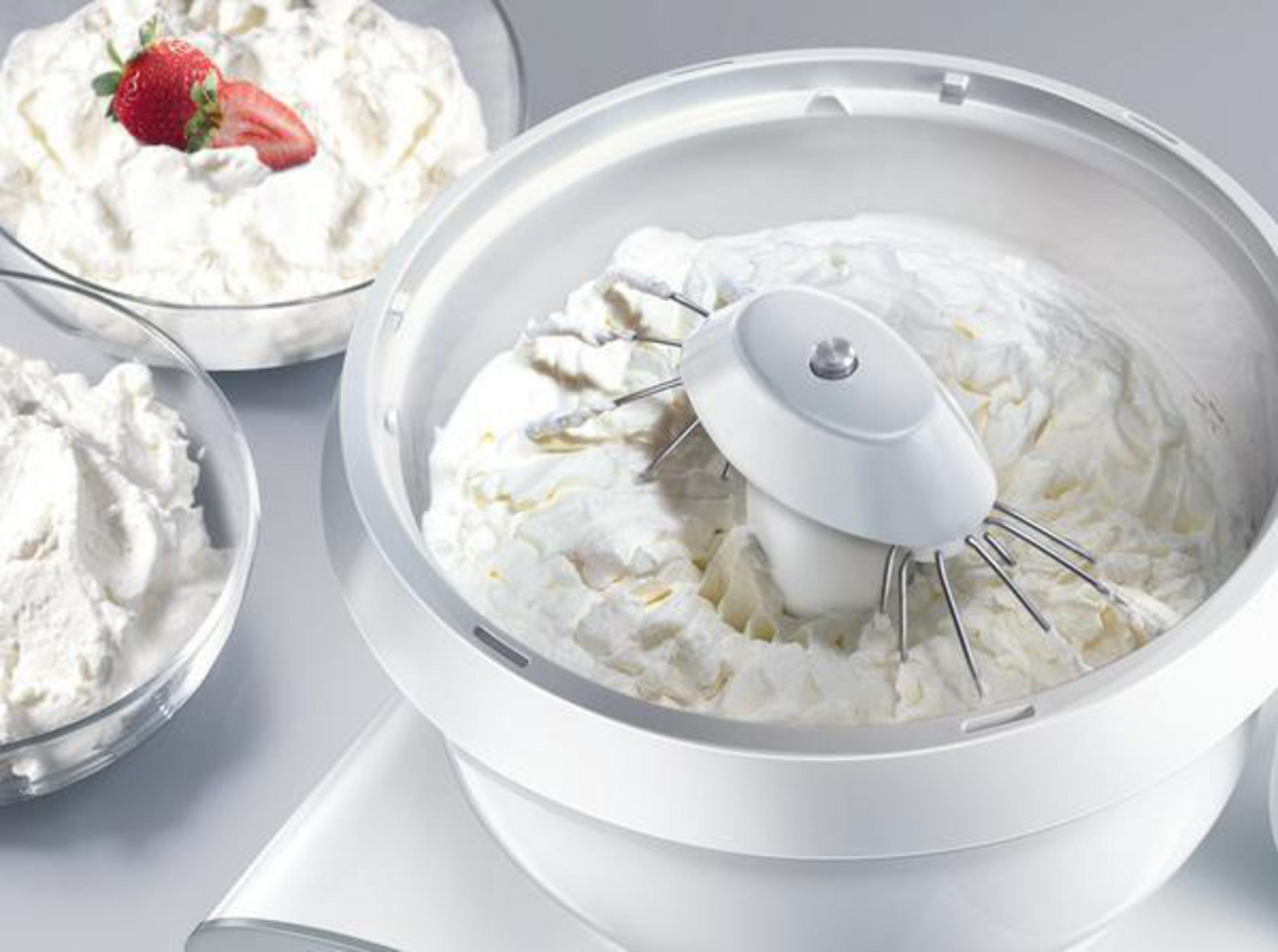 Witte mengkom met slagroom en een bevestigde mixer. Aardbeien in een kom.