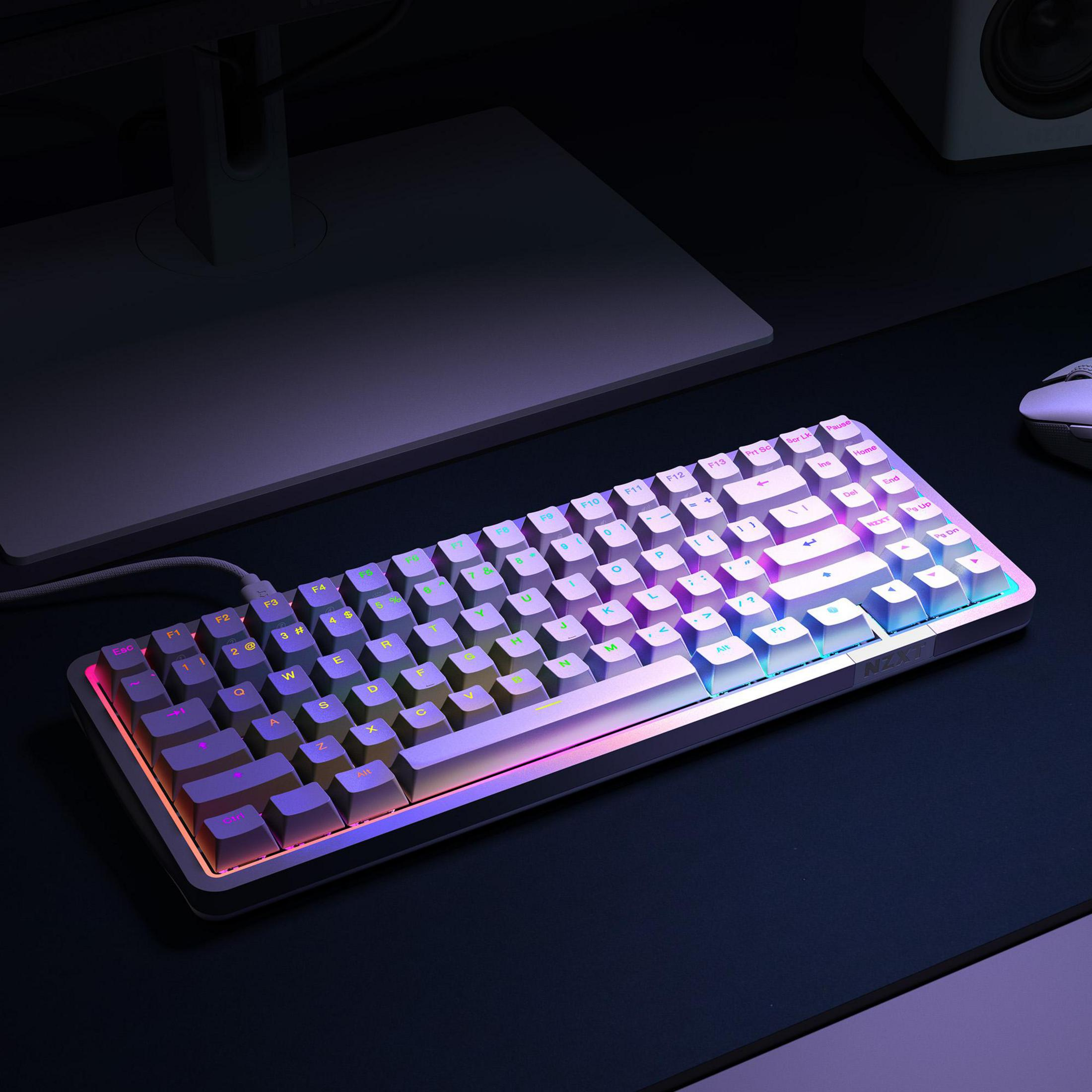 Eine beleuchtete Tastatur mit Regenbogeneffekt auf einem schwarzen Schreibtisch, ein Monitor und eine Maus im Hintergrund.