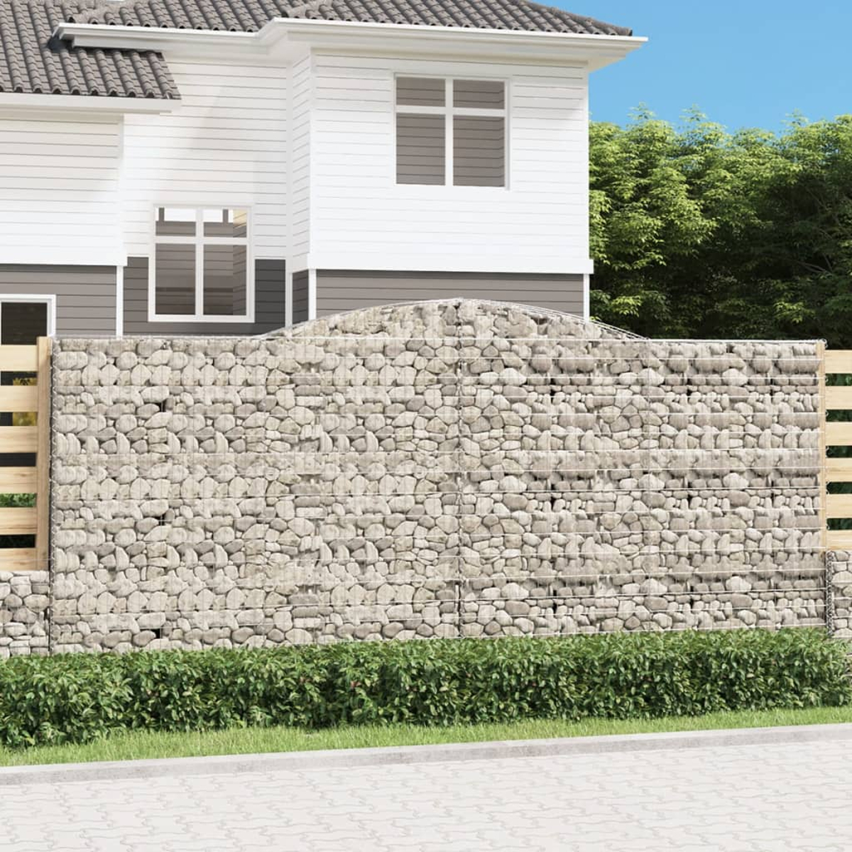Haus hinter einem Steinmauenzaun und grünen Büschen.
