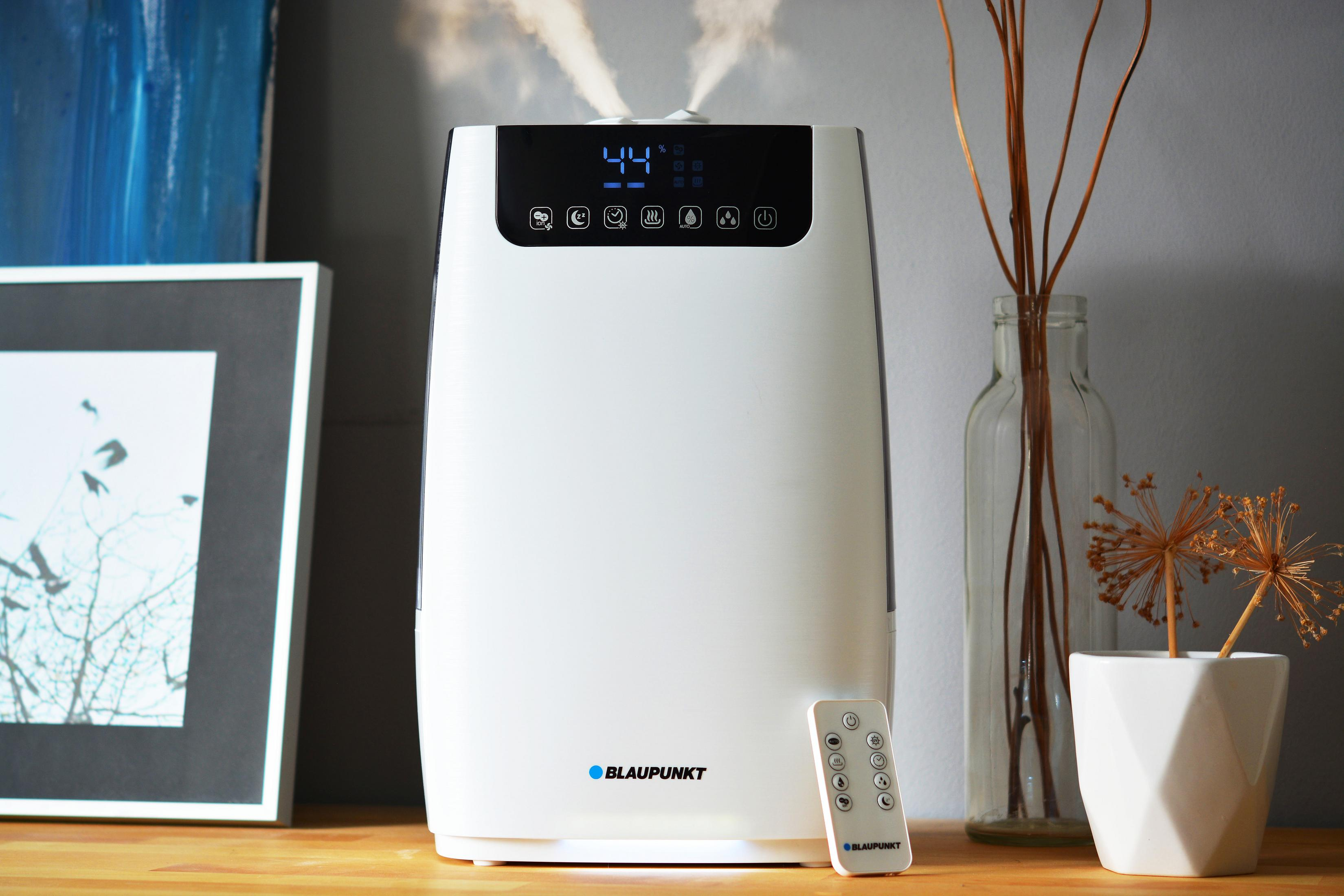 Un umidificatore Blaupunkt bianco emette vapore. È su un tavolo di legno vicino a un vaso e una cornice.