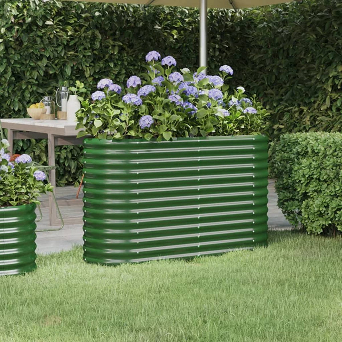 Grünes Metall-Gartenbeet mit Blumen und Grünzeug, in einer Garteneinstellung unter der Sonne.