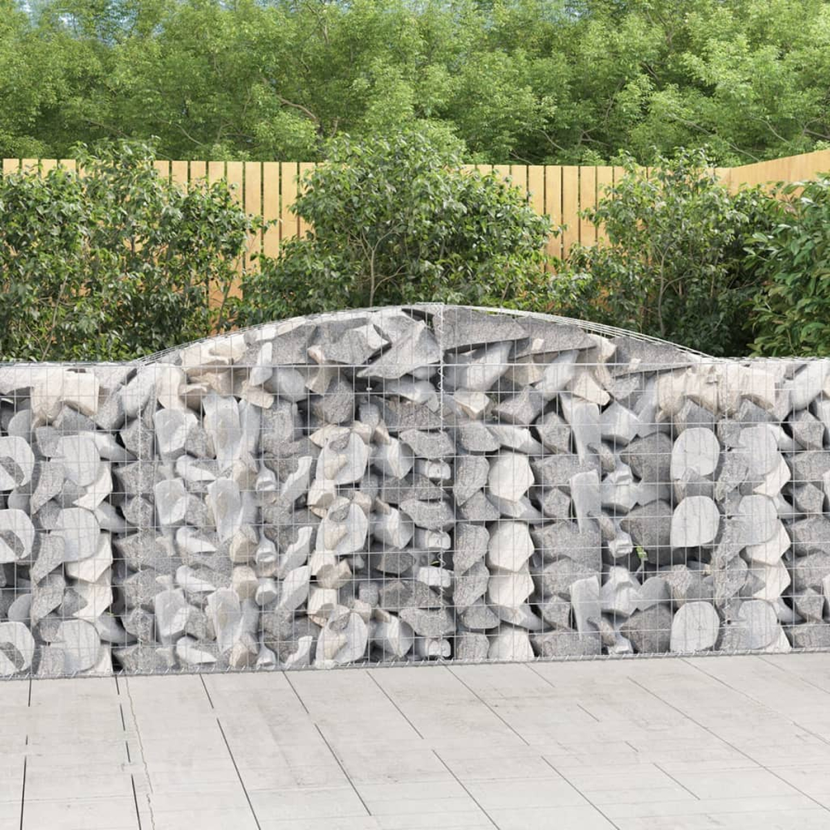 Eine Gabionenmauer mit Steinen gefüllt in einem Garten, mit Bäumen und Zaun.