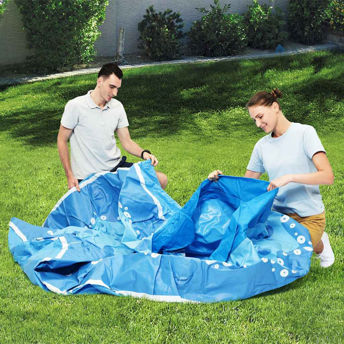 Zwei Personen bauen einen aufblasbaren blauen Pool auf einem grünen Rasen auf.