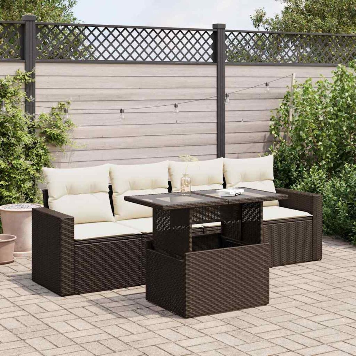 Set da patio con divano, tavolo e cuscini. Include una recinzione e vegetazione.