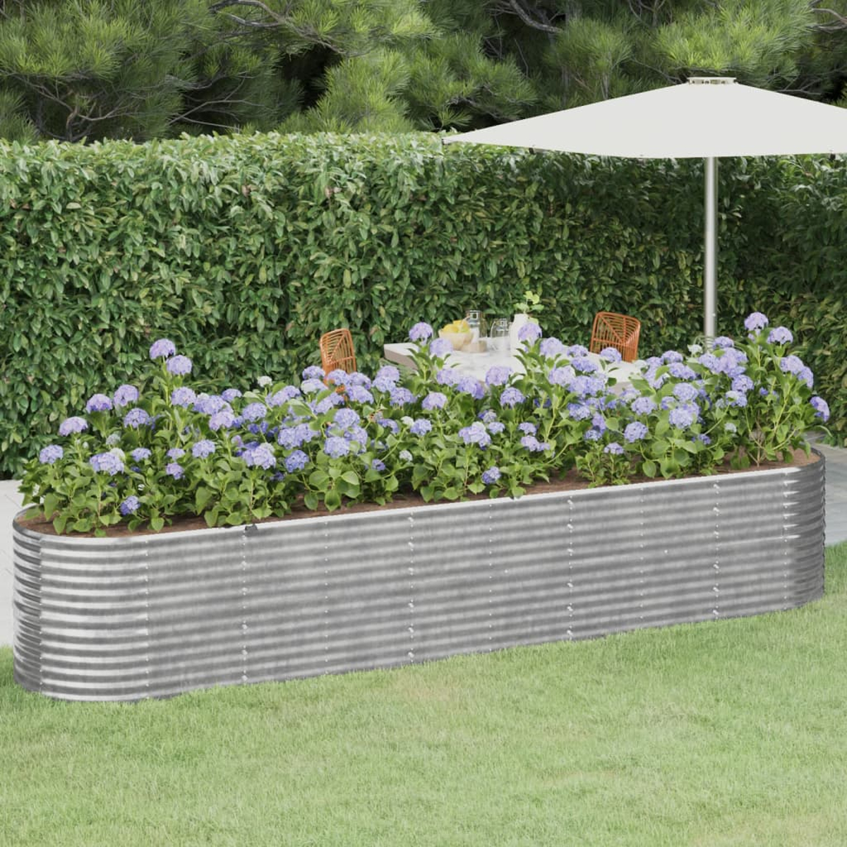 Erhöhtes Gartenbeet aus Metall, gefüllt mit blauen Blumen und grünen Pflanzen. Tisch und Stühle im Hintergrund.