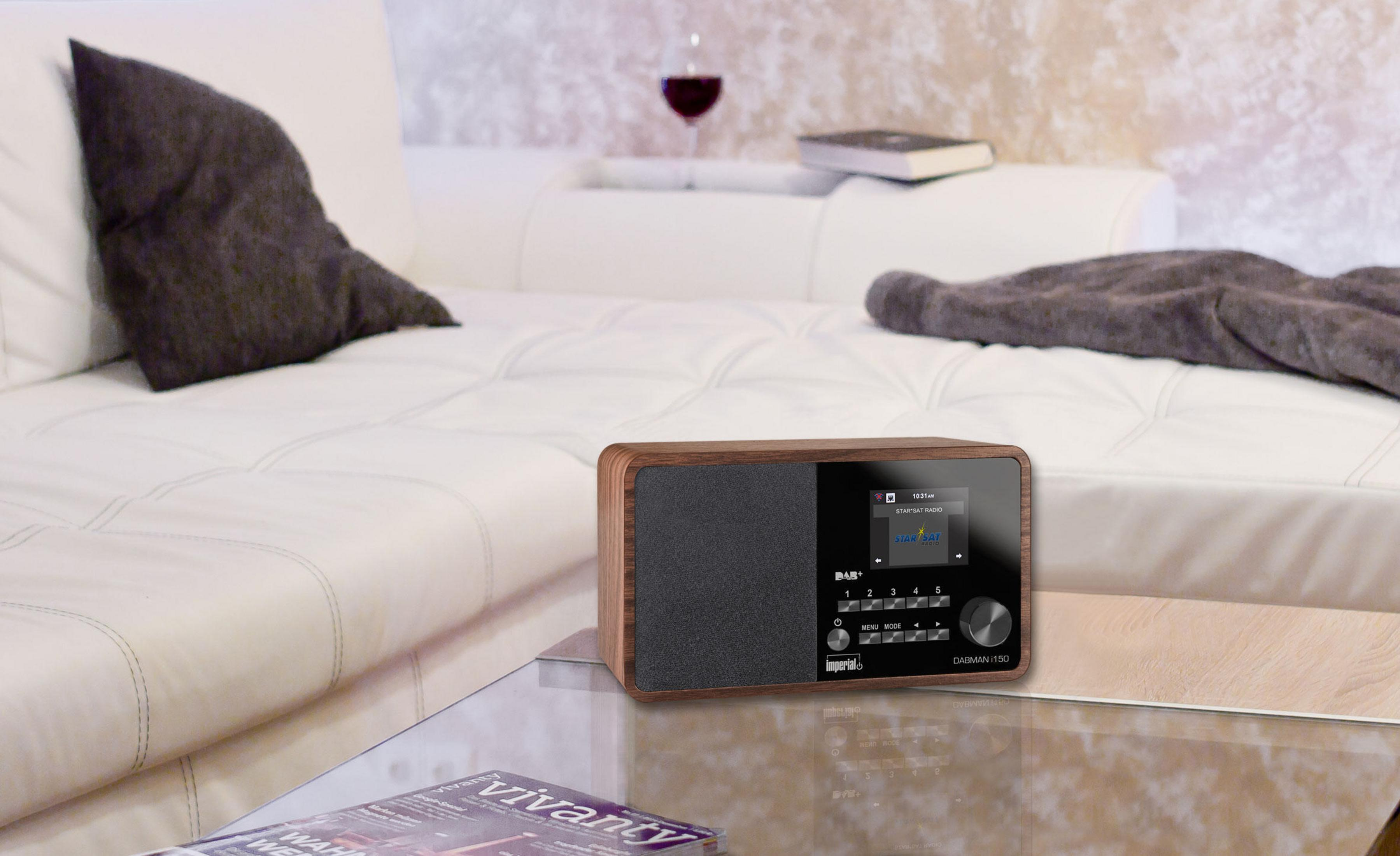 Drewniane radio z ekranem, na szklanym stole. Obecna jest szklanka wina i książka.