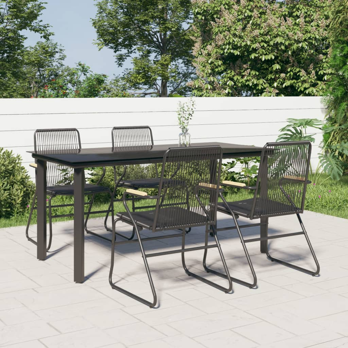 Essgruppe im Freien mit schwarzem Tisch und Stühlen auf einer Terrasse, mit Grün im Hintergrund.