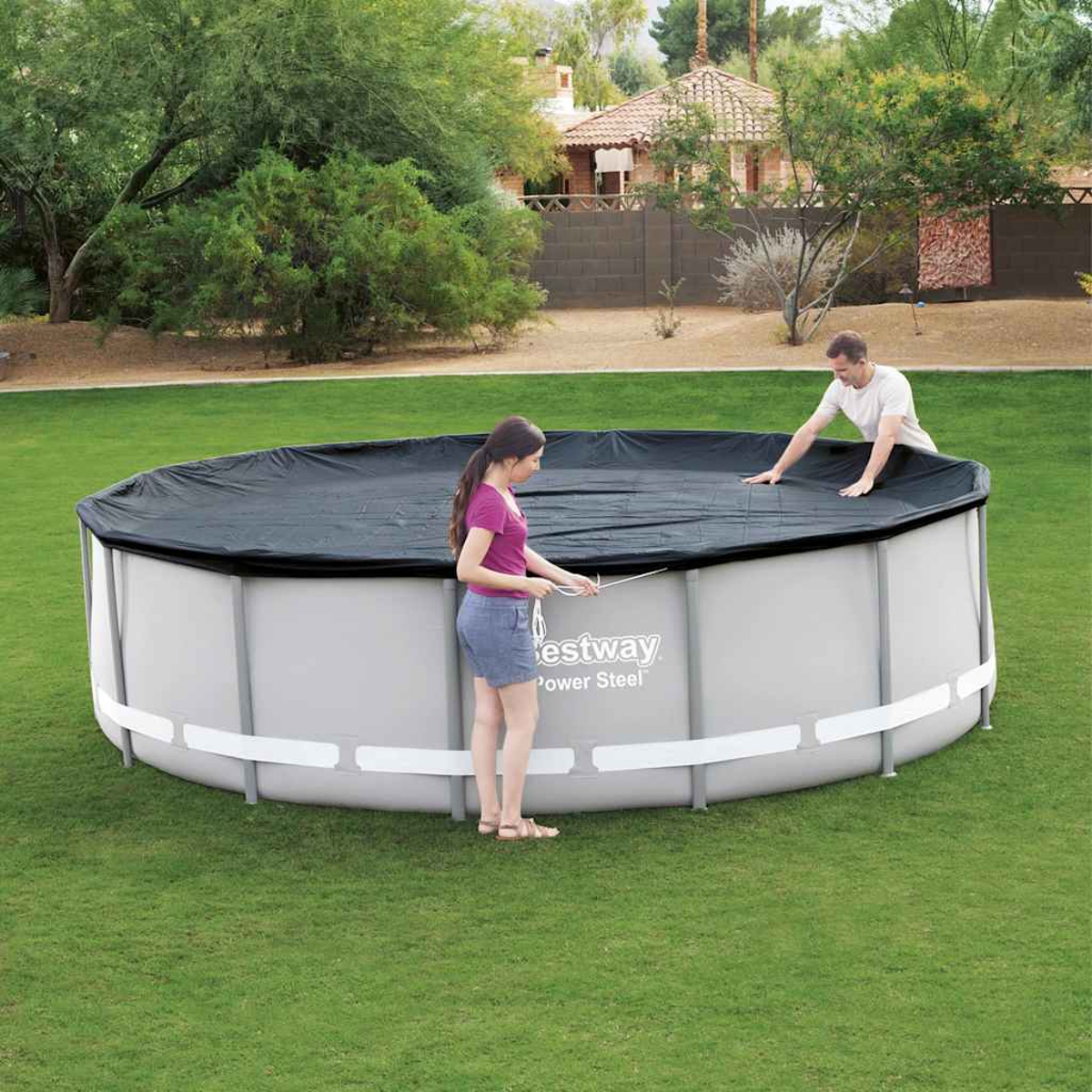 Zwei Personen bedecken einen runden, oberirdischen Pool mit einer schwarzen Abdeckung. Grünes Gras umgibt ihn.
