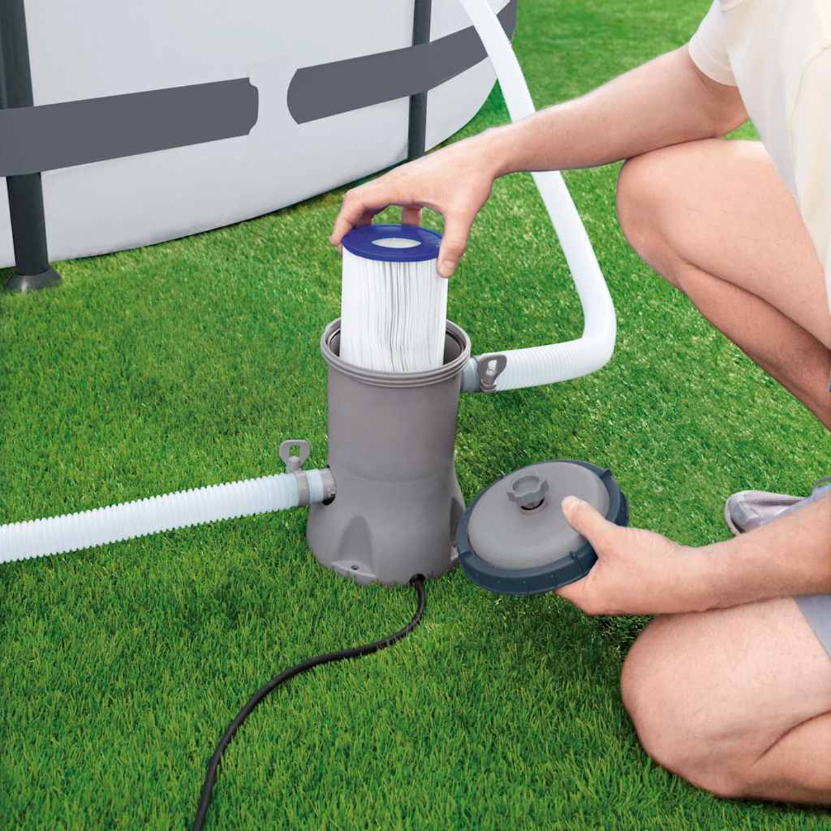 Personne ajoutant un filtre à une pompe de piscine sur de l'herbe verte.
