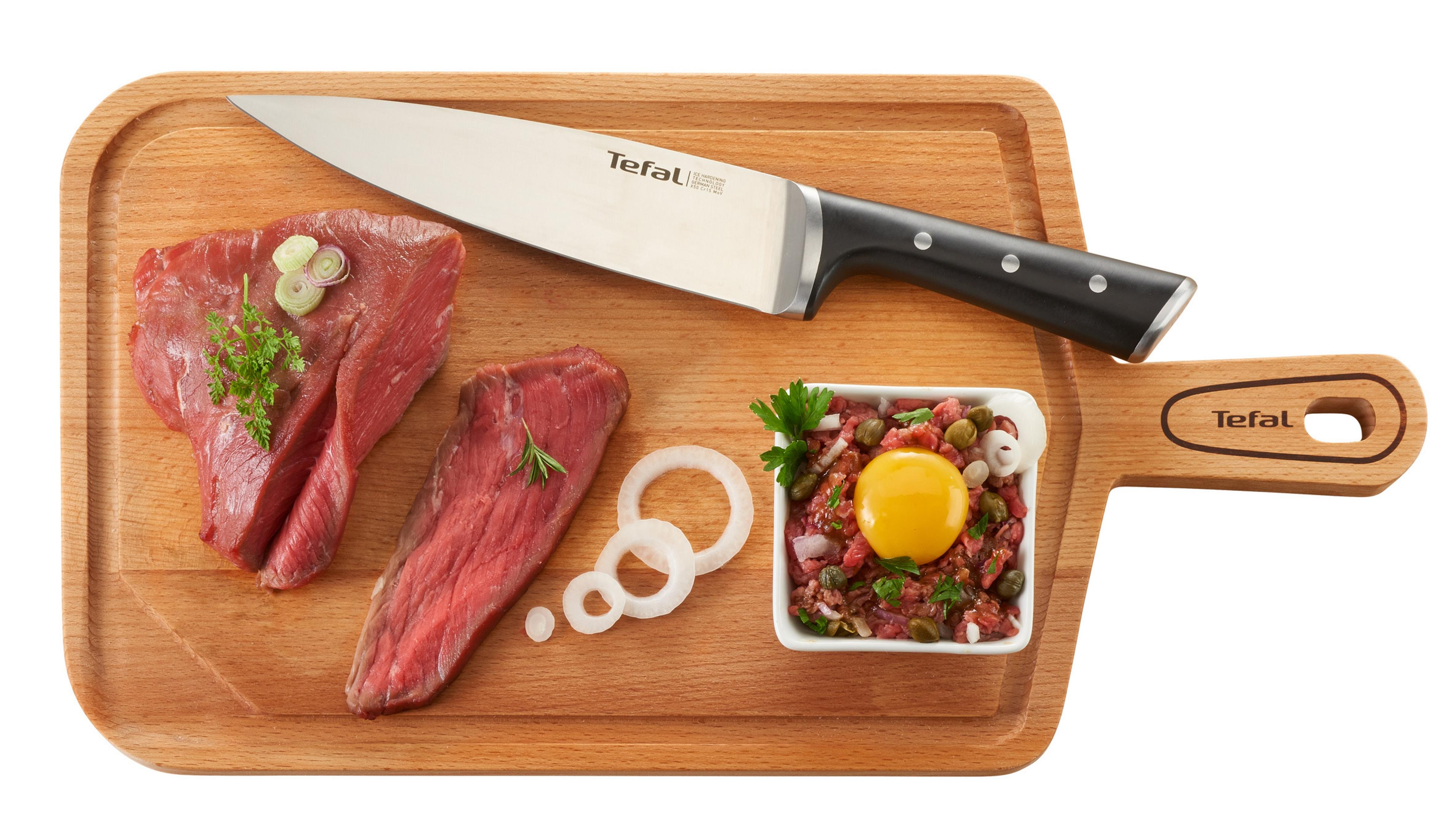 Tabla de cortar con carne cruda, cebollas y un cuenco con plato y yema de huevo.