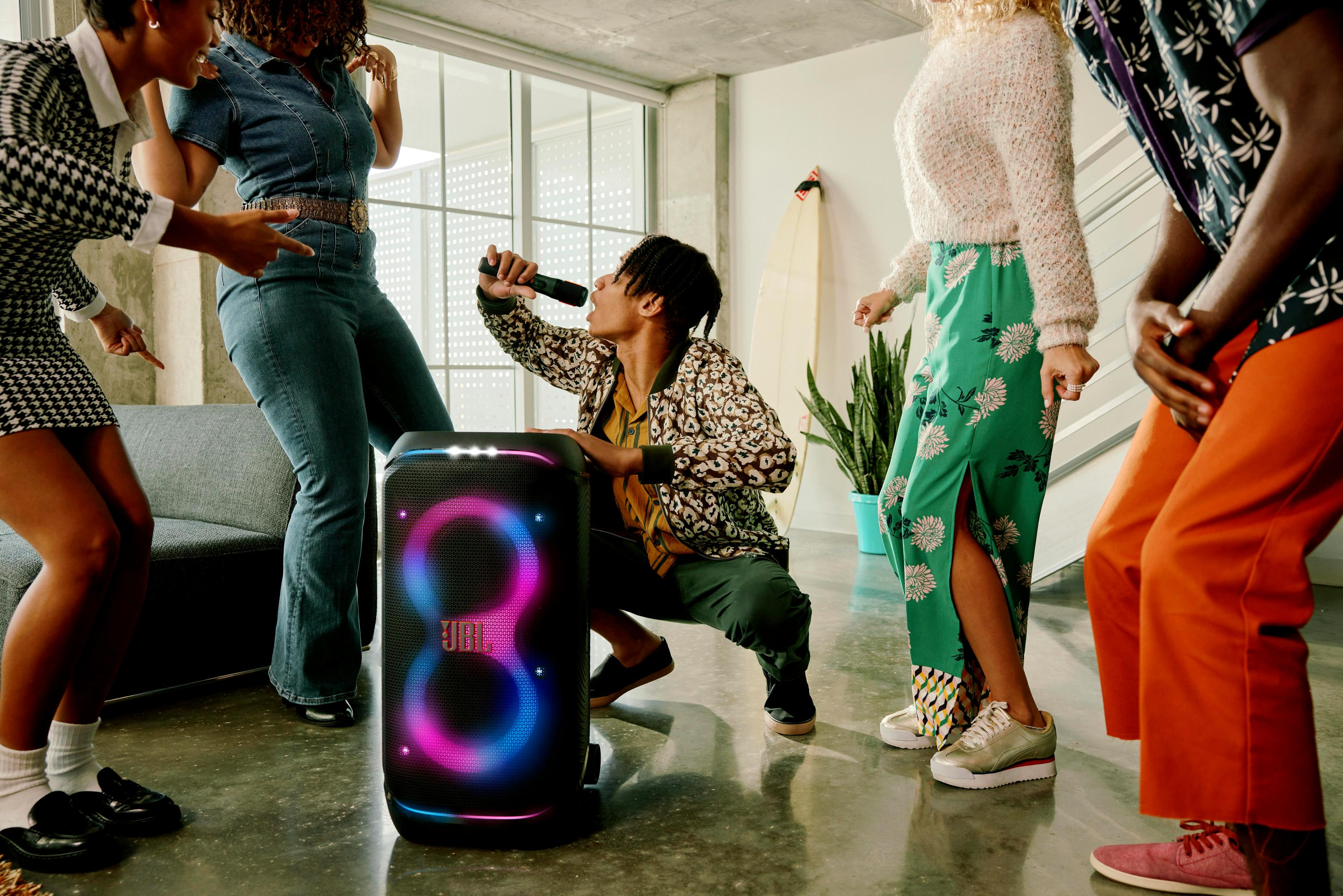 Un groupe de personnes dansant autour d'une enceinte JBL. Une personne chante dans un microphone.