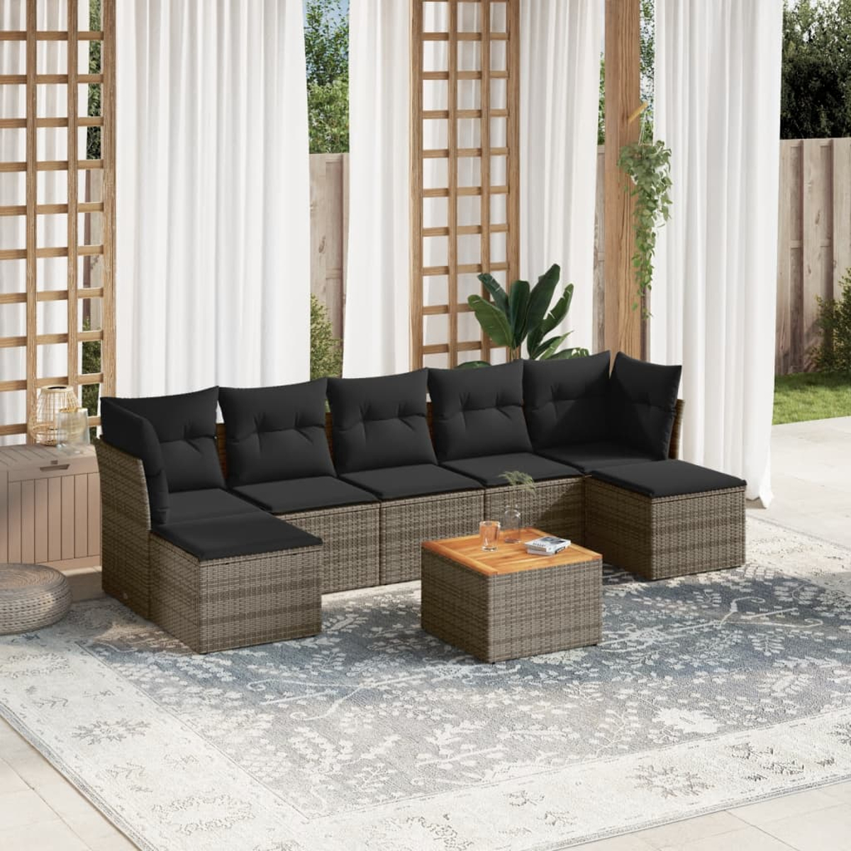 Outdoor-Rattan-Sofagarnitur mit schwarzen Kissen und einem Couchtisch auf einem Teppich.