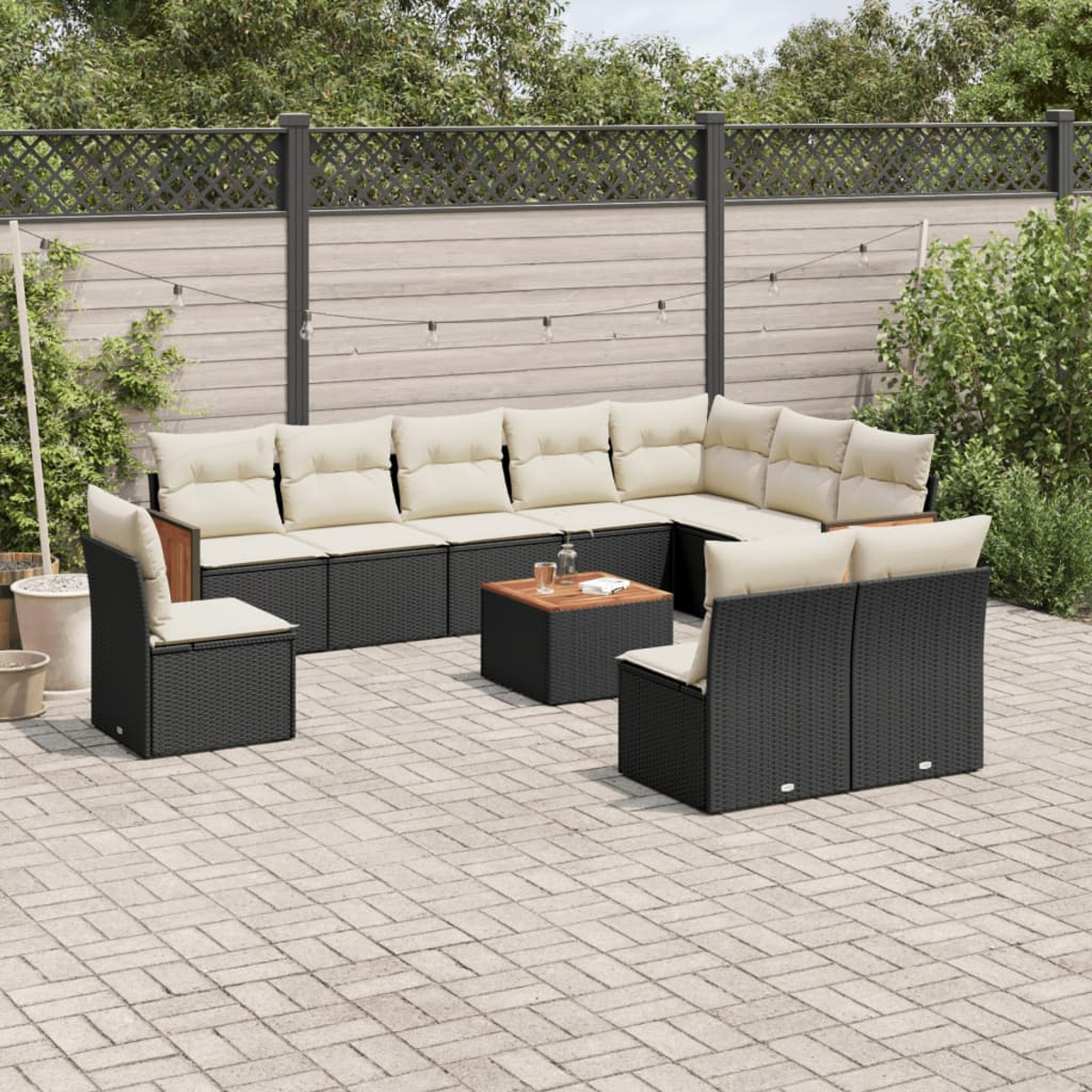 Un set da patio all'aperto con mobili in vimini neri e cuscini beige, in un giardino.