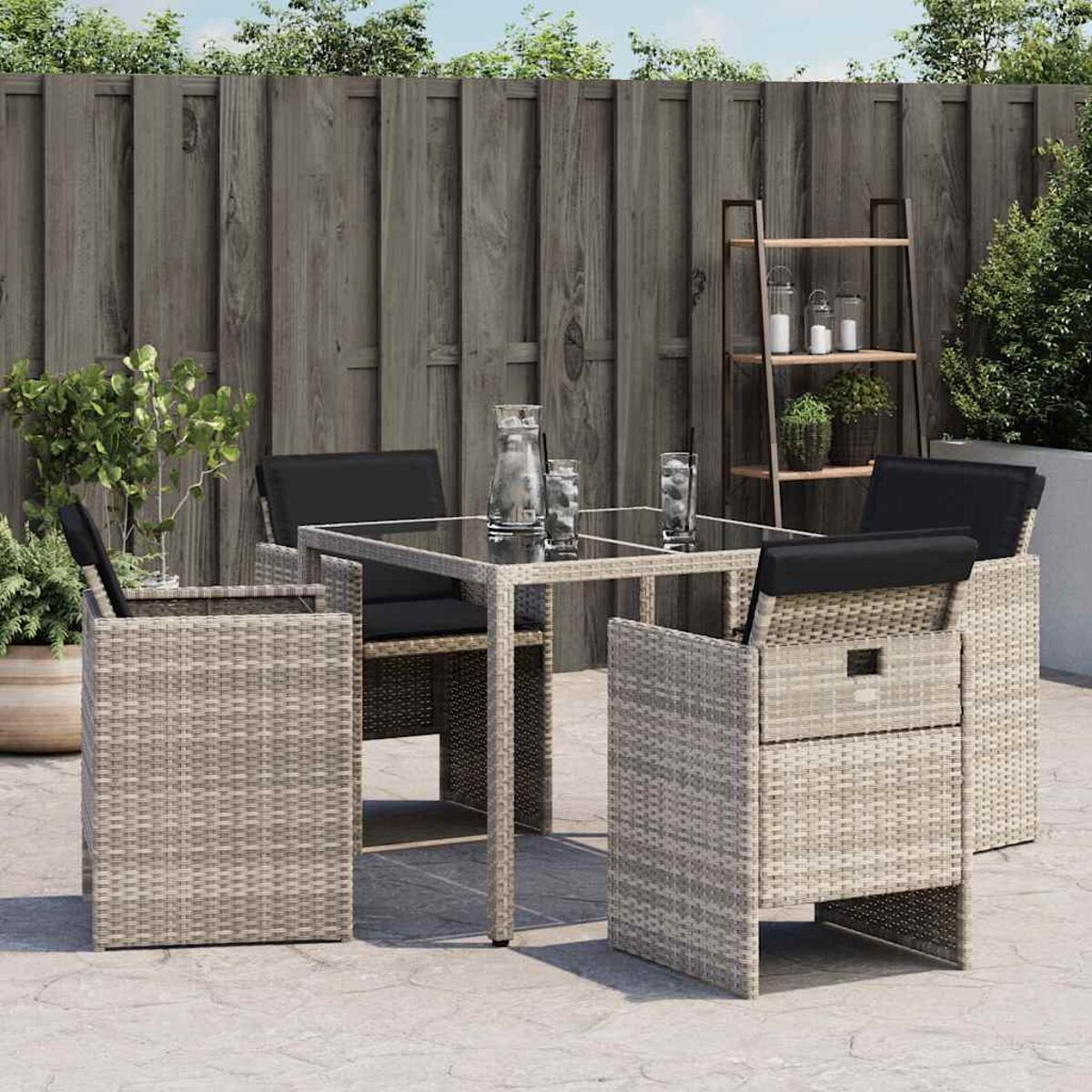 Ein Outdoor-Terrassenset mit einem Tisch und vier Stühlen. Die Stühle haben schwarze Kissen und ein gewebtes Design.