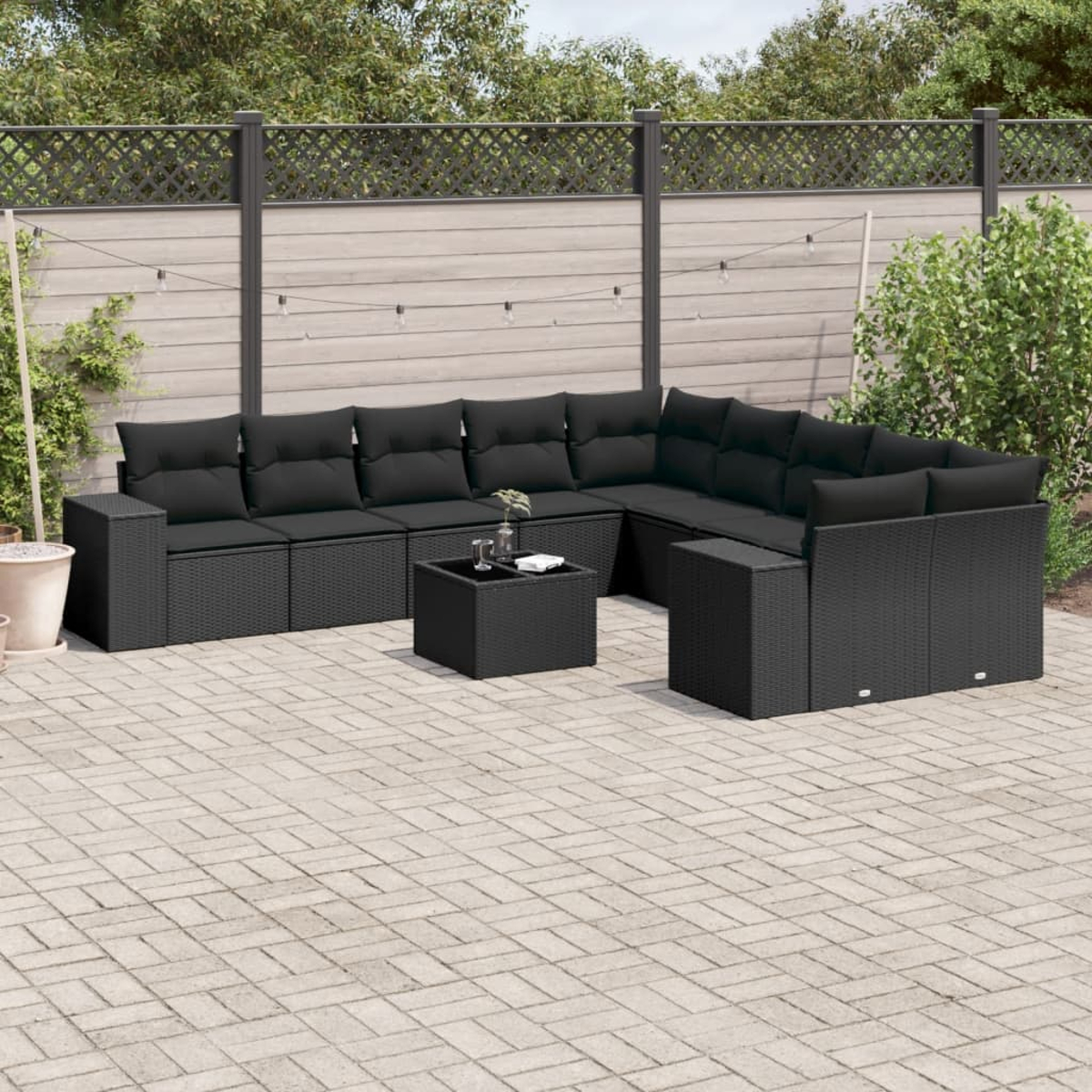Schwarzes Outdoor-Geflechtmöbel-Set. Enthält Ecksofa, Couchtisch und Kissen. Ziegelpflaster, Holzzaun.