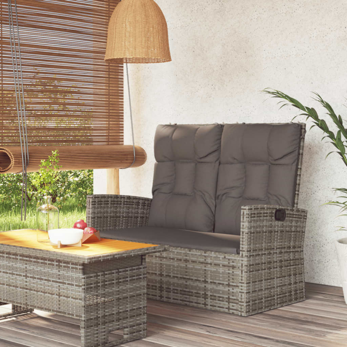 Rattan-Liebesitz mit grauen Kissen und einem Holztisch. Auf einem Holzdeck mit einem Fenster im Hintergrund.