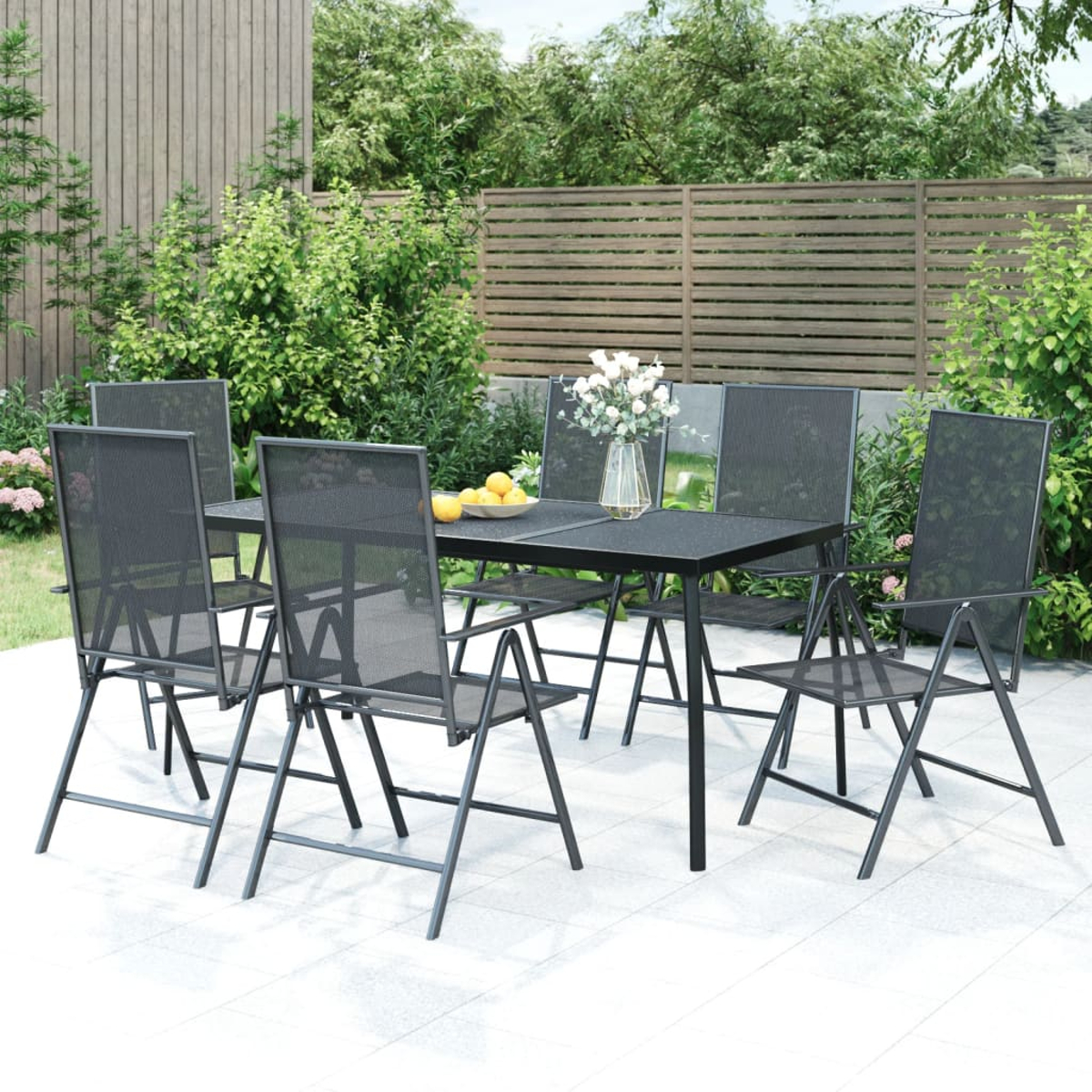 Essgruppe im Freien: Tisch und sechs Stühle auf einer Terrasse mit Pflanzen im Hintergrund.