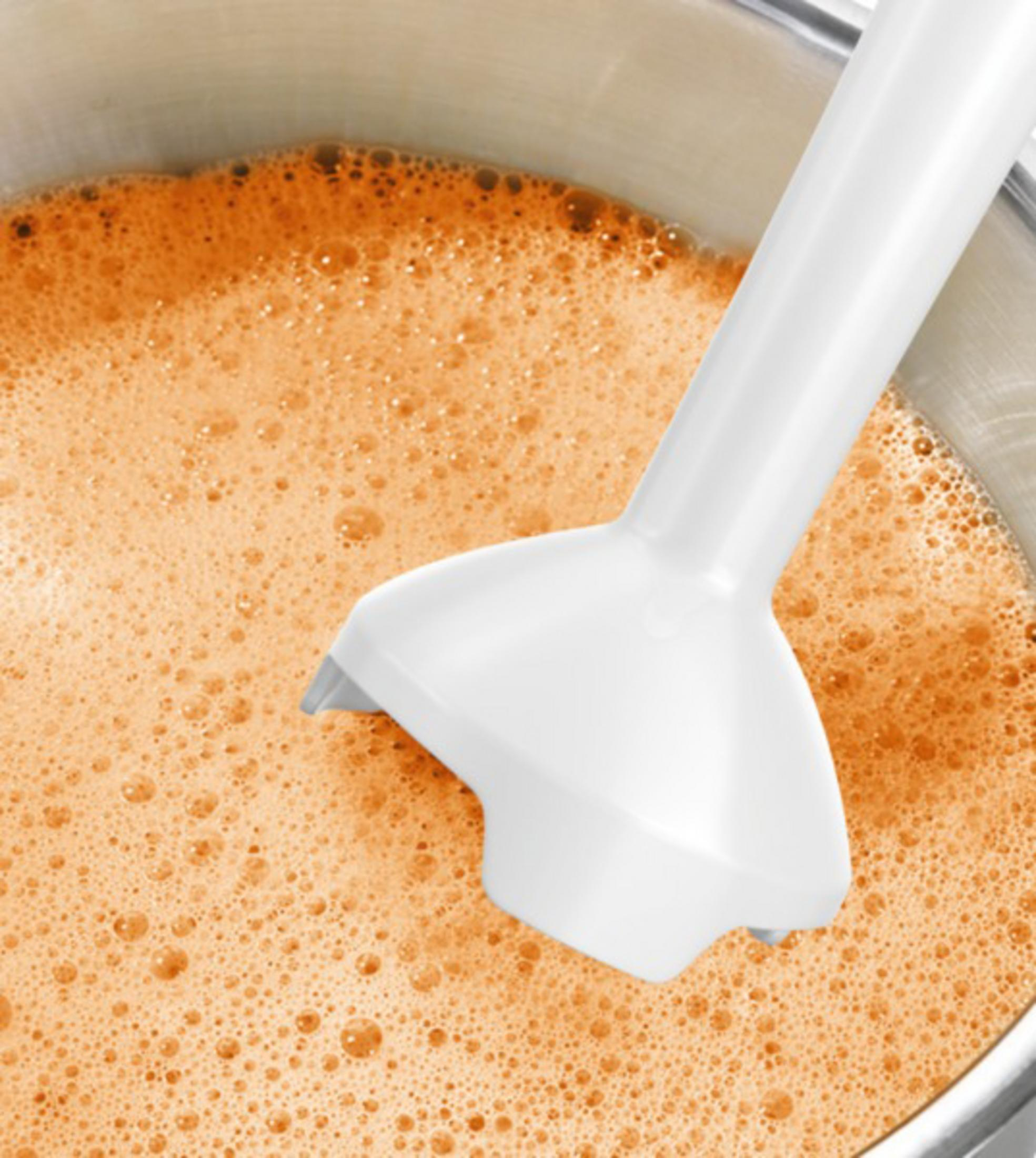 Ein weißer Mixerkopf in einem Topf mit orangener Flüssigkeit. Die Flüssigkeit hat viele kleine Blasen.