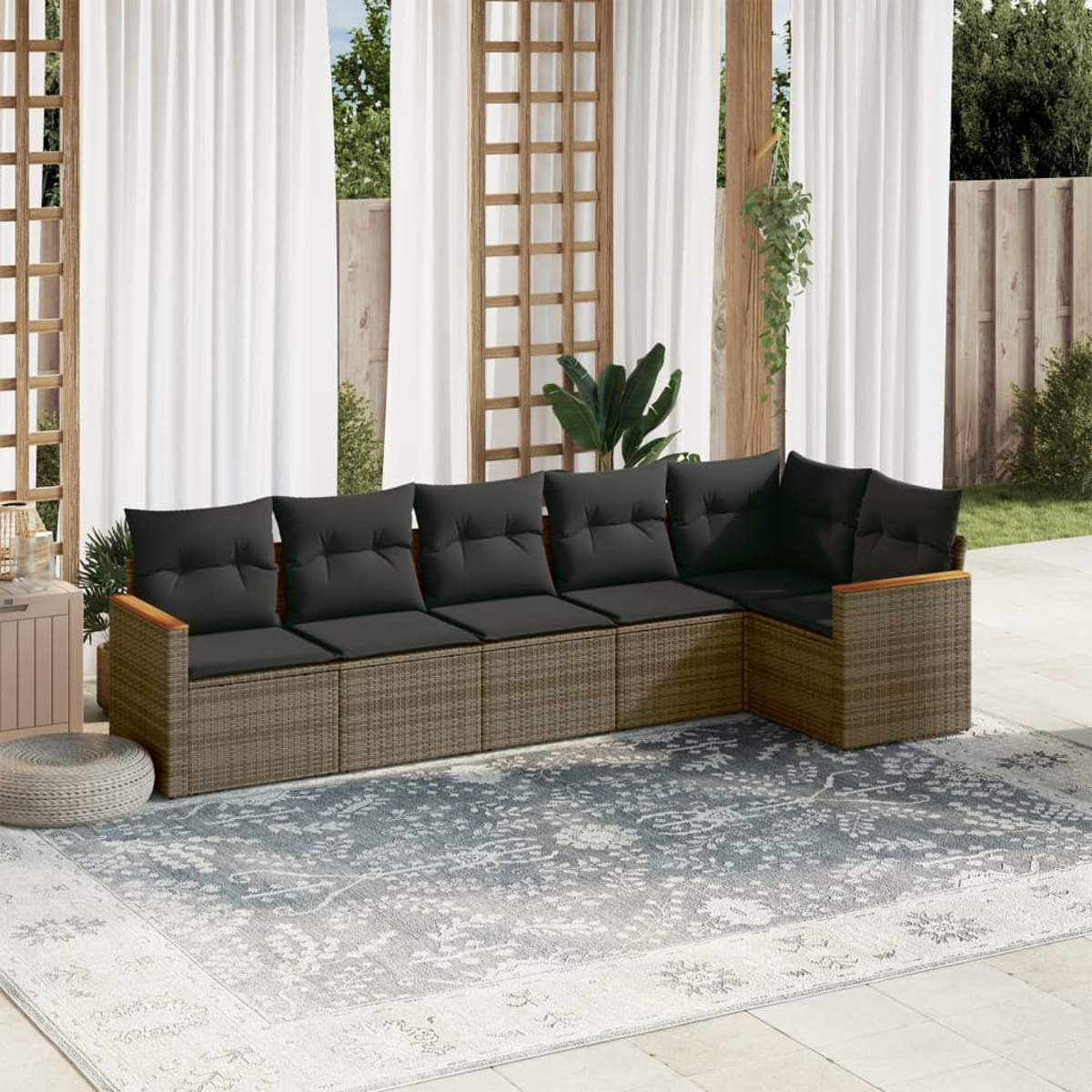 Outdoor-Ecksofa mit schwarzen Kissen auf einem gemusterten Teppich. Weiße Vorhänge, Holzrahmen und grüne Pflanzen im Hintergrund.