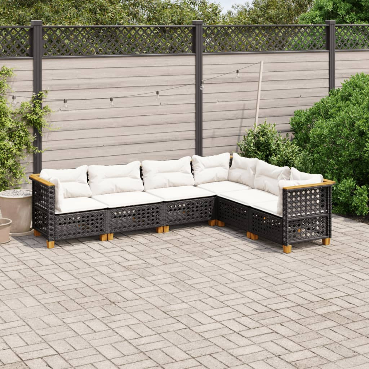 Schwarzes Outdoor-Ecksofa mit weißen Kissen. Das Sofa steht auf einer Backstein-Terrasse, mit einem Zaun im Hintergrund.