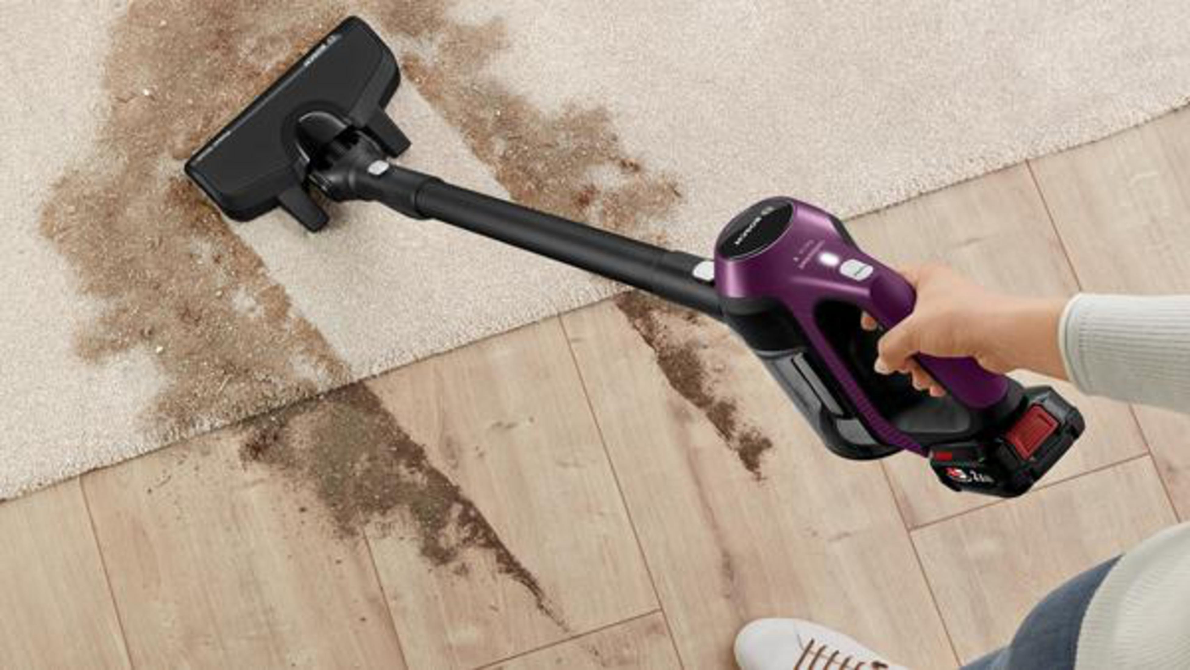 Una persona che aspira un pavimento in moquette con un aspirapolvere viola senza fili.