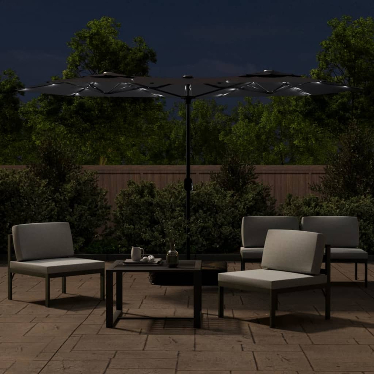 Außenszene bei Nacht mit Stühlen, Tisch und Sonnenschirm. Dunkler Himmel, grüne Pflanzen und ein beleuchteter Bereich auf einer Terrasse.