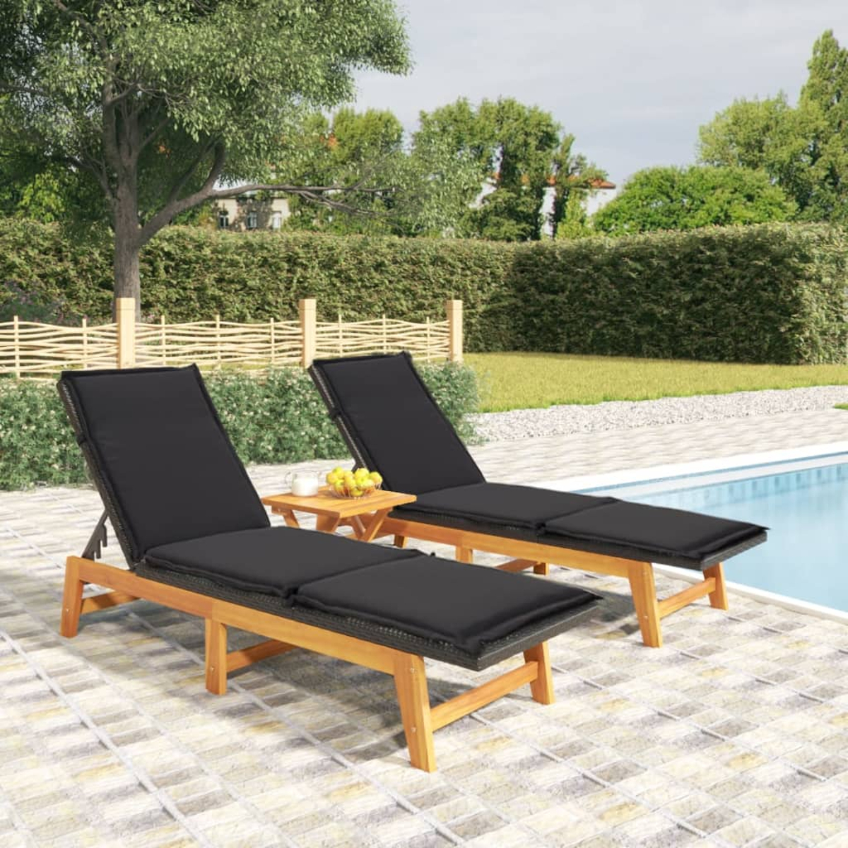 Zwei Liegestühle aus Holz mit schwarzen Polstern neben einem Tisch mit Obst, am Pool.