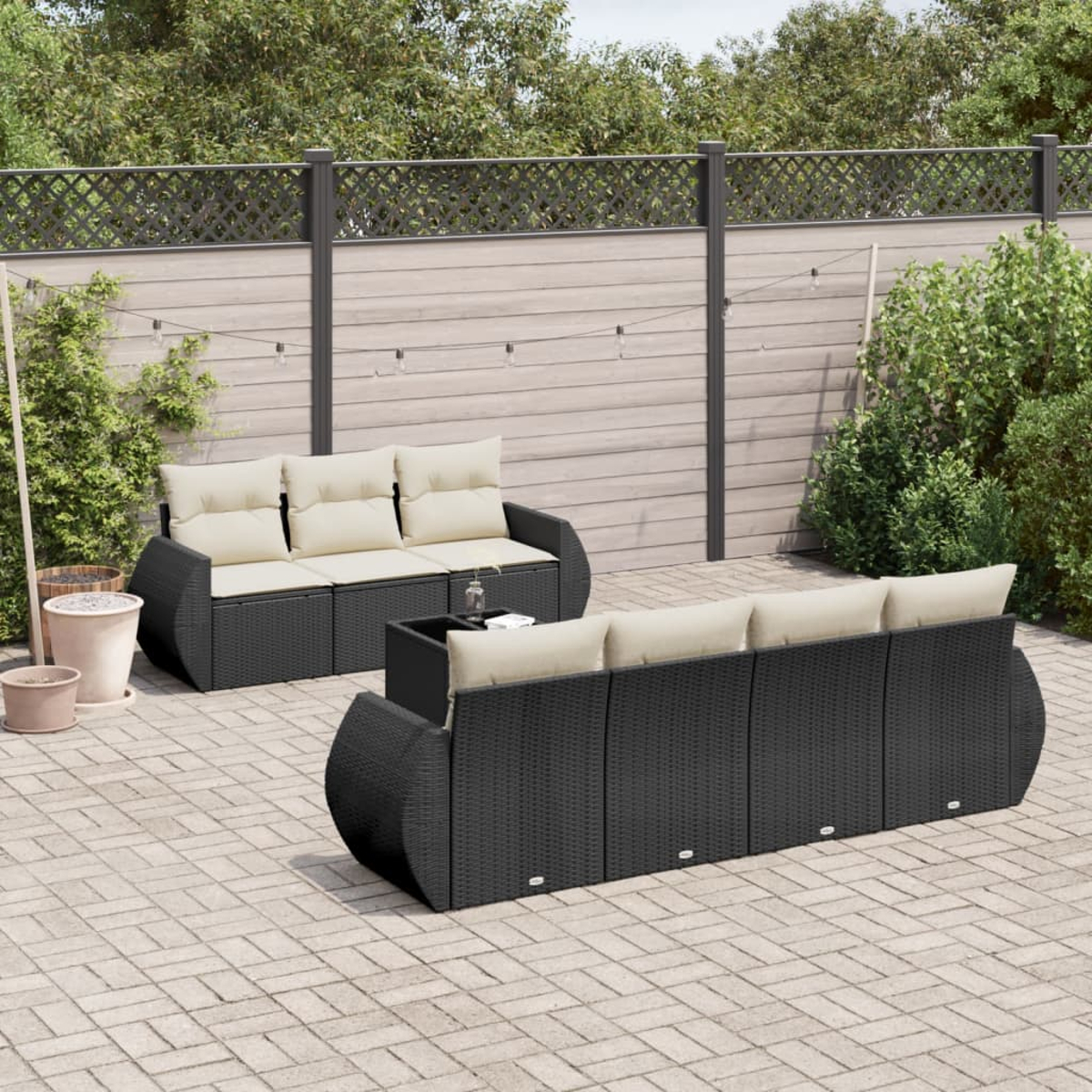 Outdoor-Sitzgruppe mit schwarzen Kissen und einem kleinen Tisch. Die Umgebung befindet sich auf einer Terrasse, mit grünem Hintergrund.