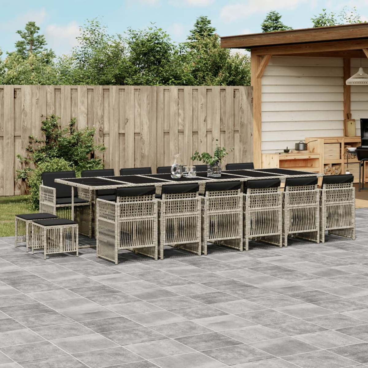 Essgruppe im Freien auf einer Terrasse. Langer Tisch mit Stühlen, ein kleiner Tisch und ein Holzzaun im Hintergrund.
