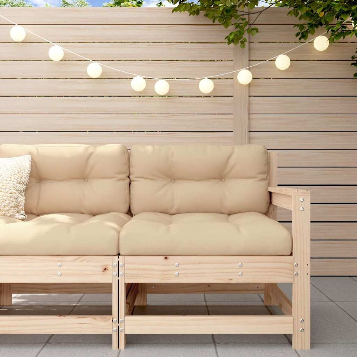 Holz-Außencouch mit beigen Kissen. Lichterkette und Holzzaun im Hintergrund.