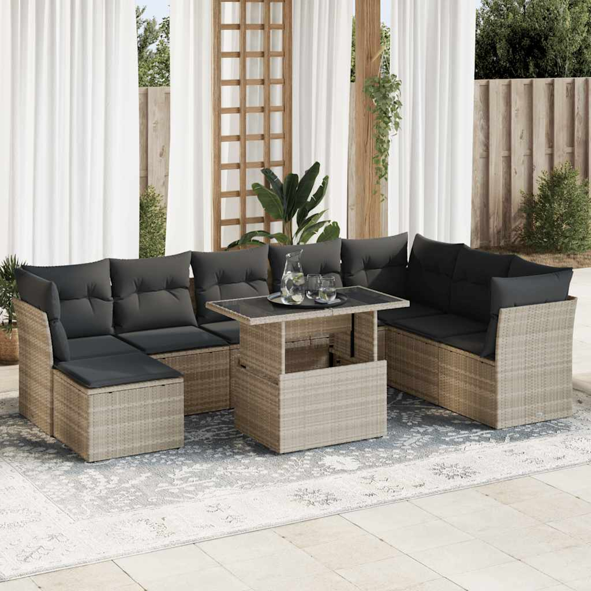 Set di mobili da esterno in rattan con tavolo e sedute componibili con cuscini grigi, su sfondo luminoso.