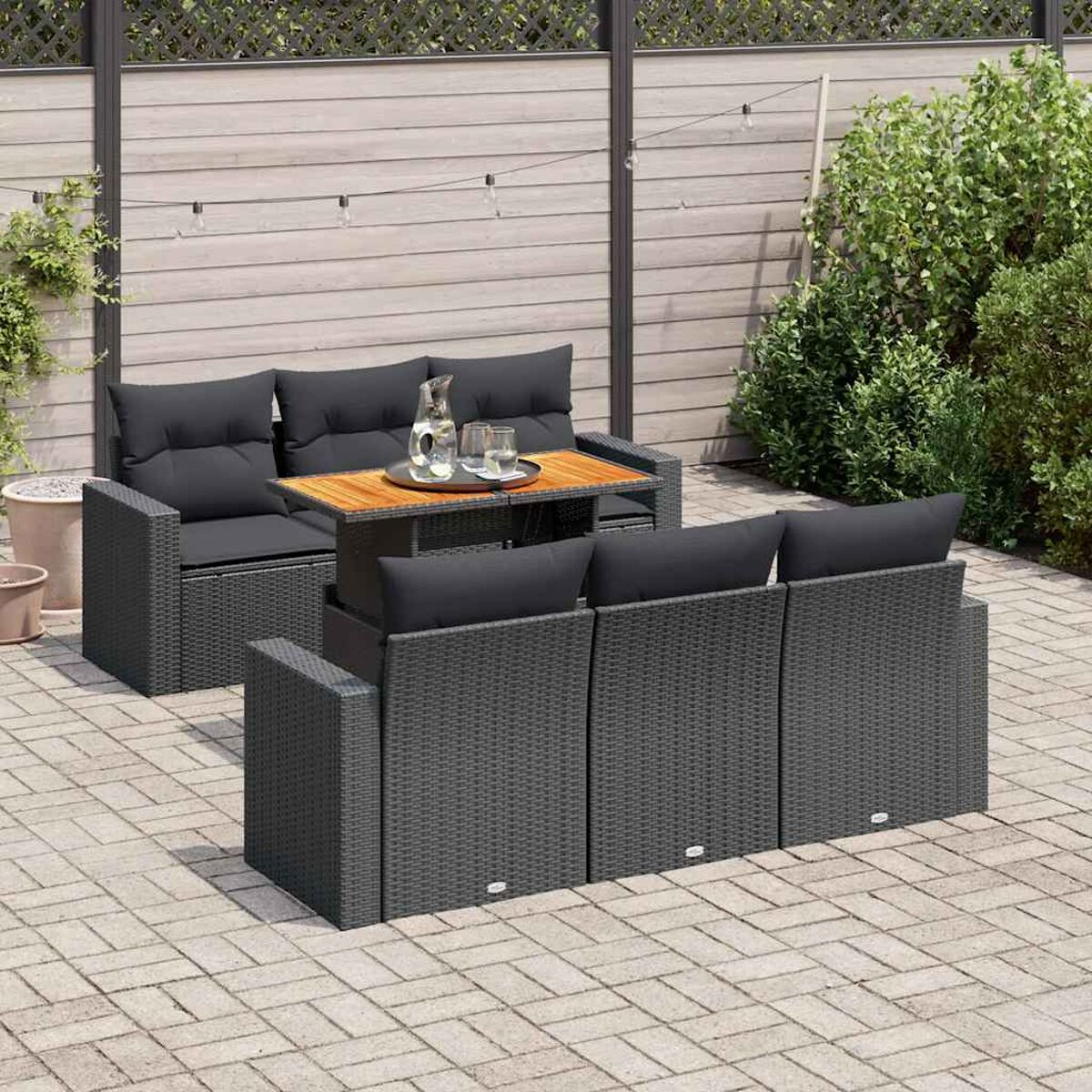 Set di mobili da esterno in rattan grigio con tavolo e cuscini su un patio in mattoni con piante.