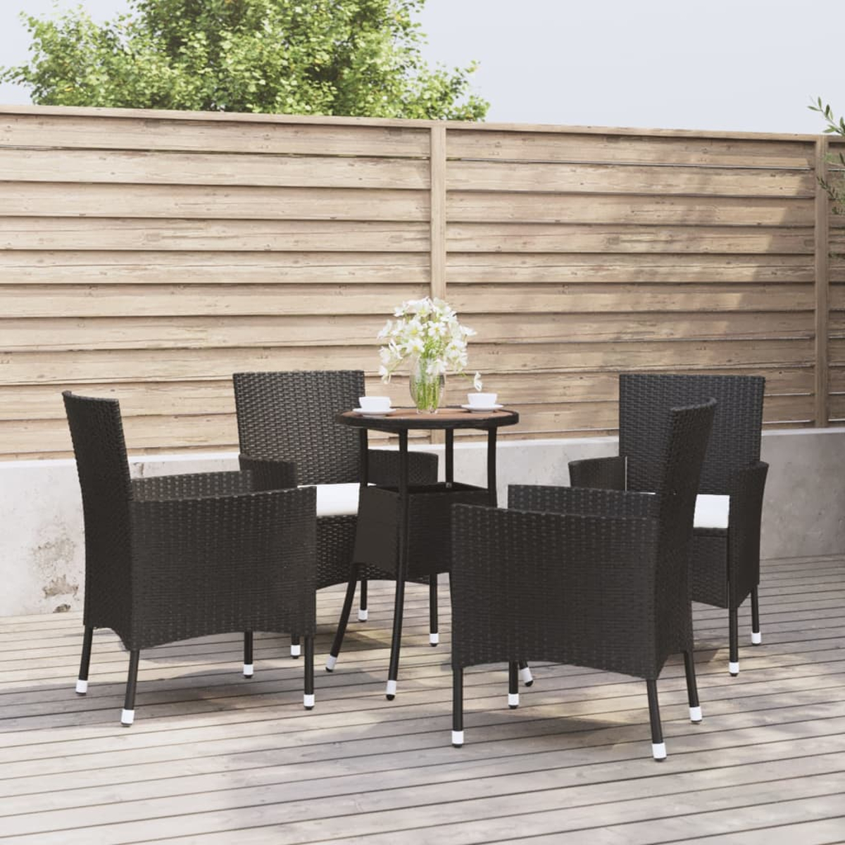 Outdoor-Essgruppe auf einer Holzterrasse. Enthält einen Tisch und vier schwarze Korbstühle. Hintergrund Holzzaun.