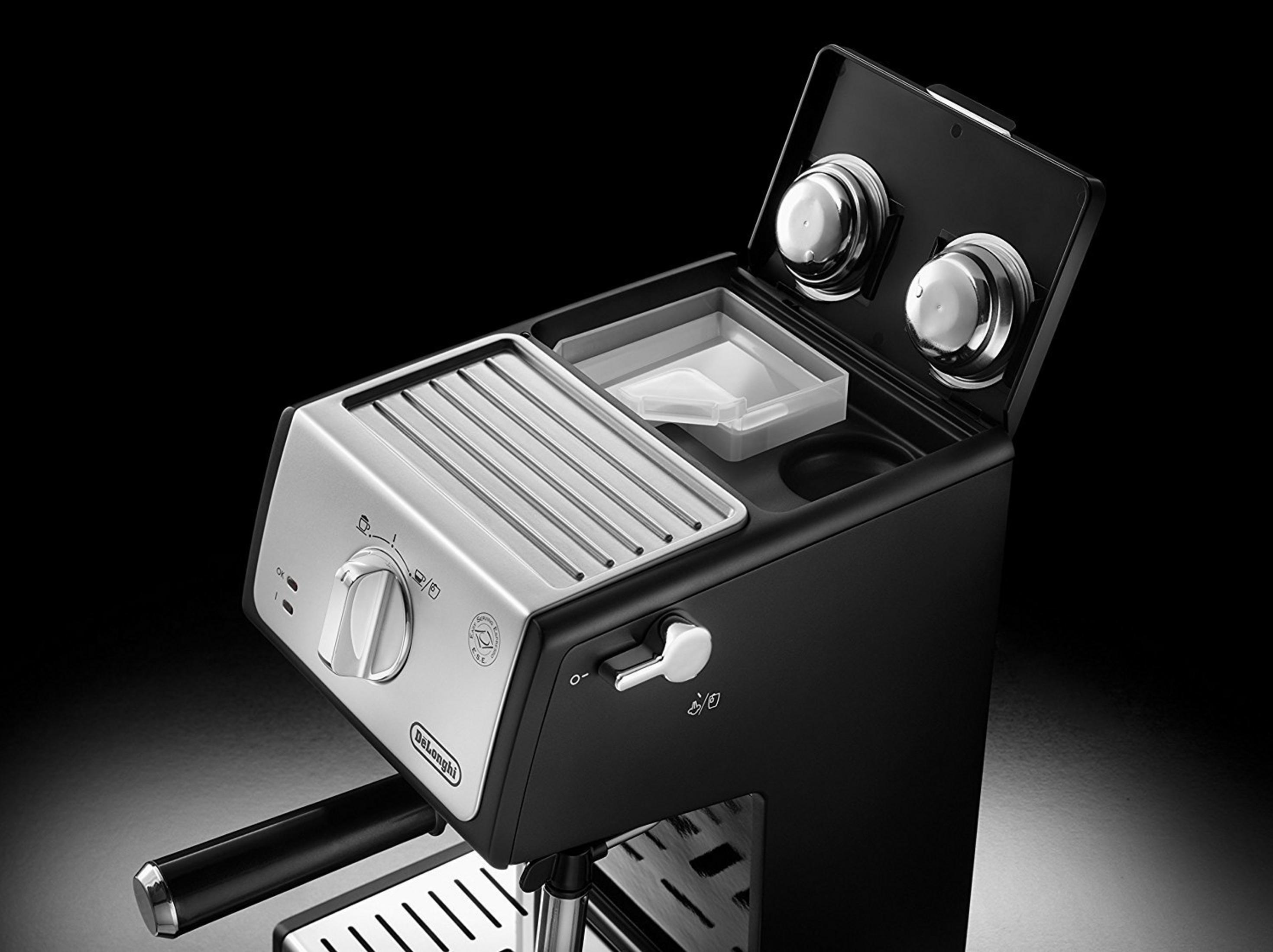 Czarny i srebrny ekspres do espresso. Górna komora jest otwarta. Tło jest czarne.