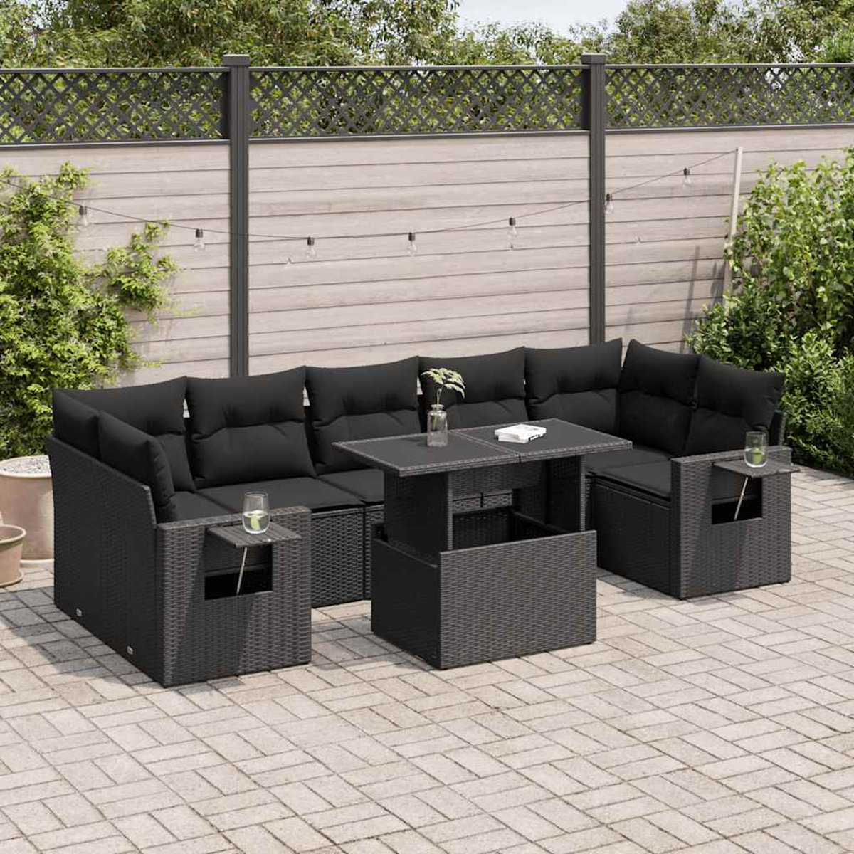 Un set da esterno in vimini con tavolo e cuscini neri, su un patio in pietra.